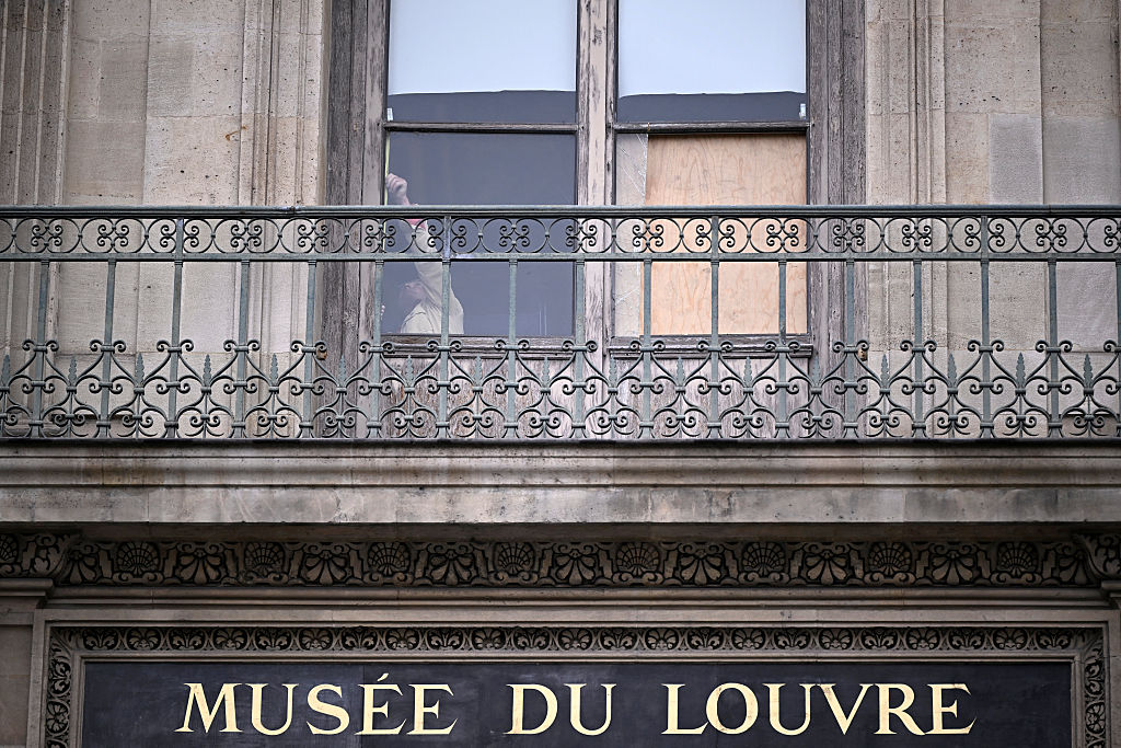 Eine Person steht hinter dem Fenster, durch das die Diebe eingestiegen sind, die am Vortag acht unbezahlbare königliche Schmuckstücke aus dem Louvre-Museum gestohlen haben, in Paris am 20. Oktober 2025. | Quelle: Getty Images