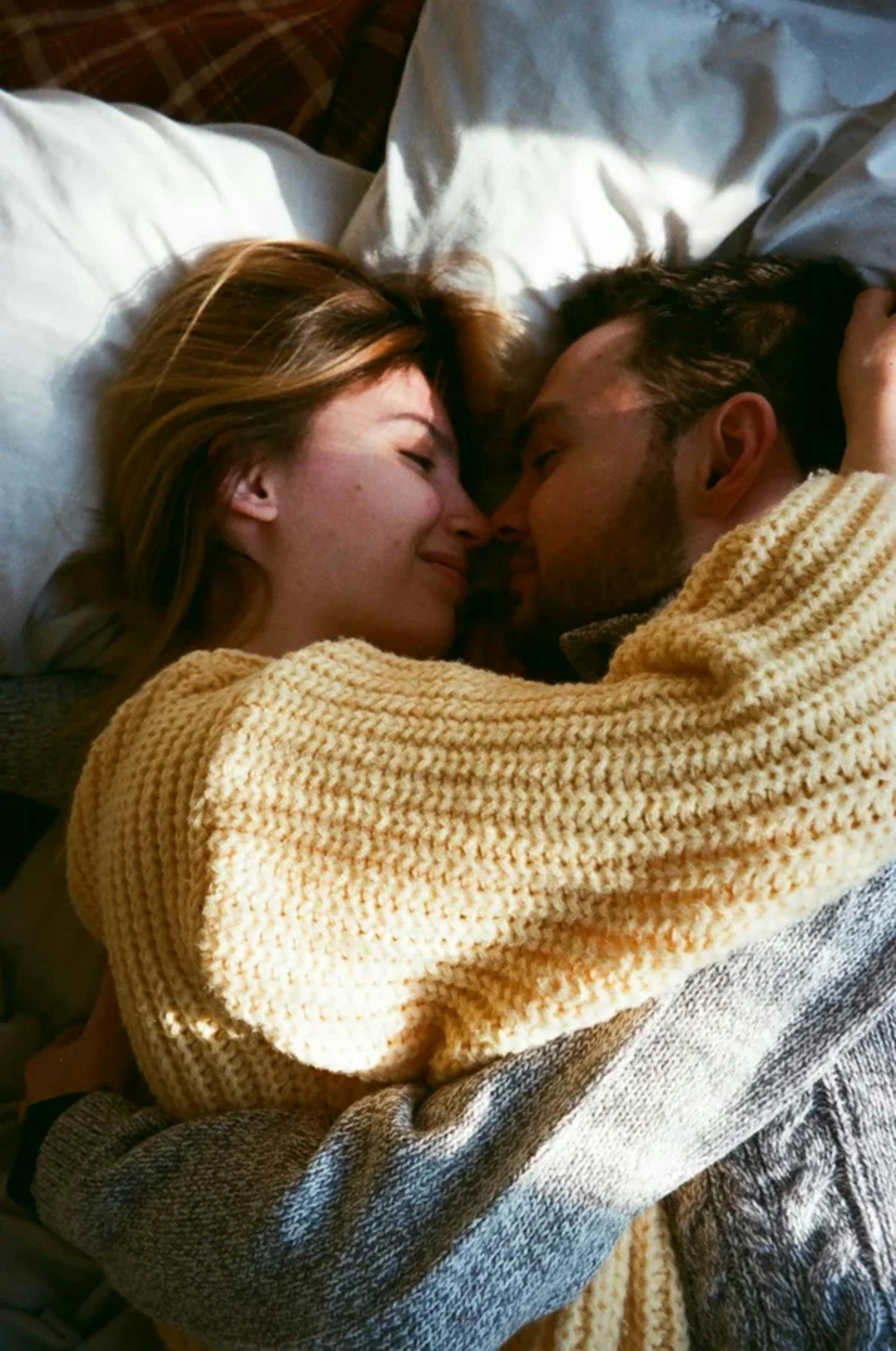 Ein glückliches Paar in Pullovern, das auf einem Bett liegt und sich umarmt | Quelle: Pexels
