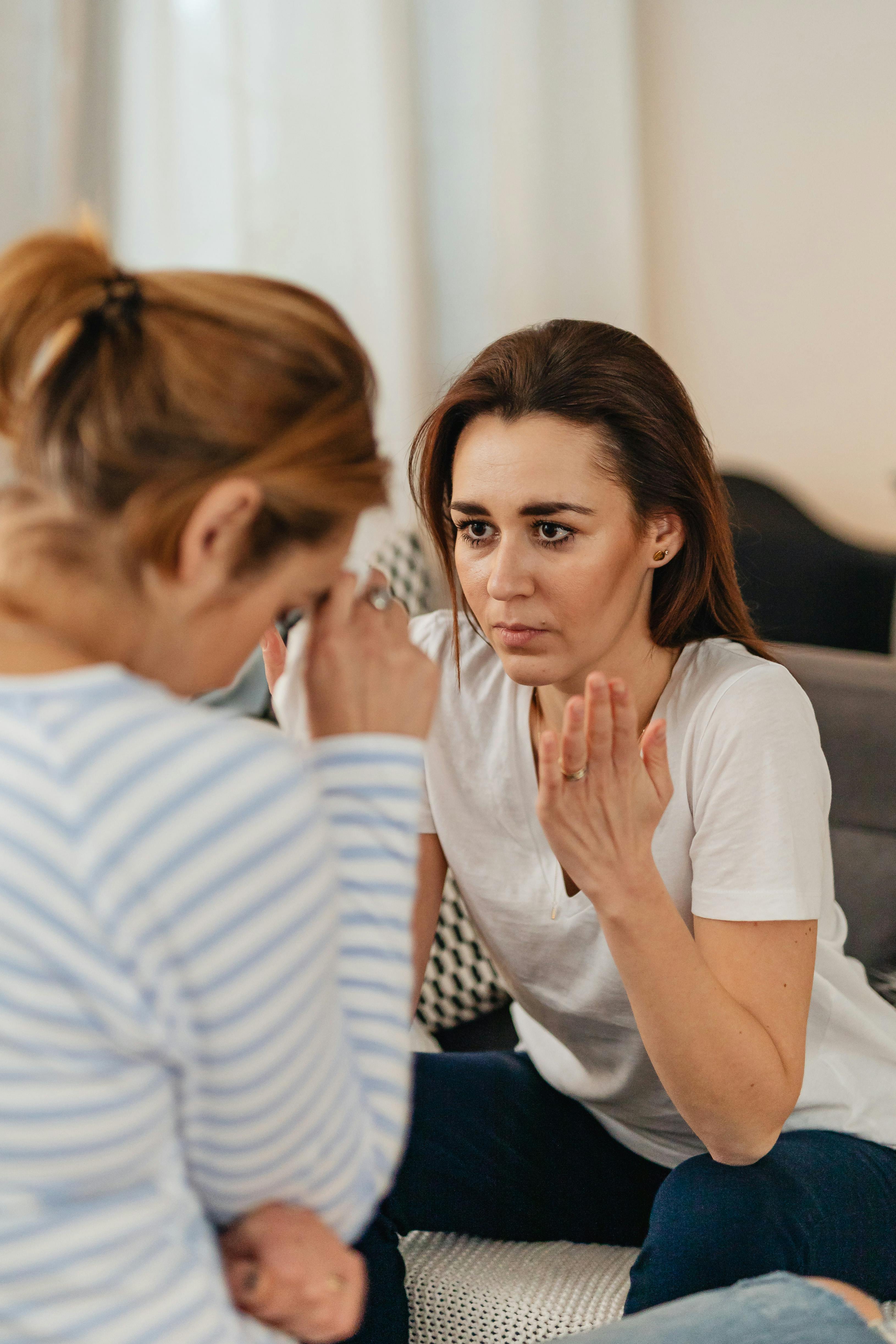 Eine Frau spricht, während eine andere ihr Gesicht senkt | Quelle: Pexels