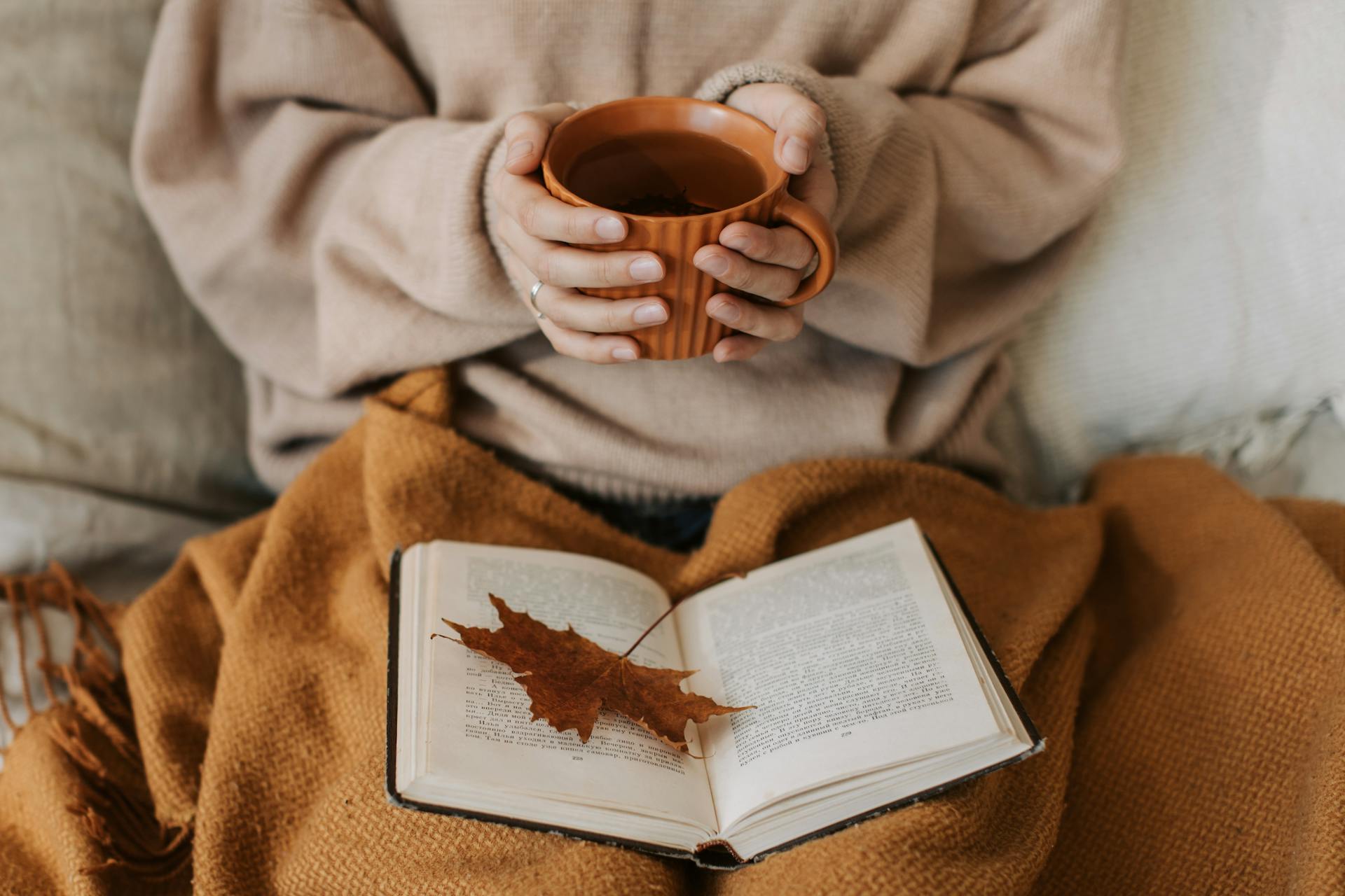 Nahaufnahme einer Frau, die ein Buch liest, während sie eine Tasse Tee in der Hand hält | Quelle: Pexels