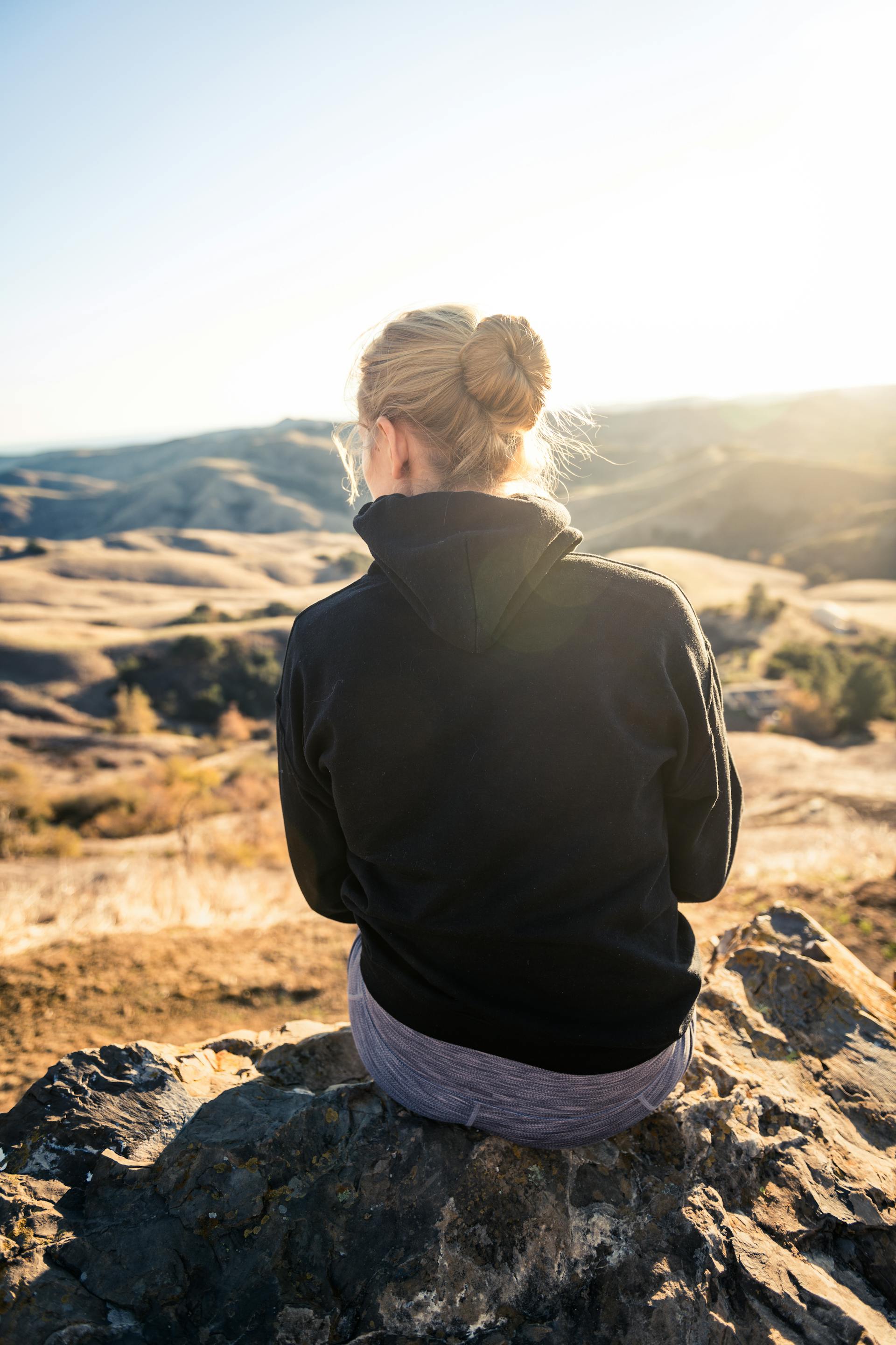 Frau im schwarzen Kapuzenpulli sitzt auf einem Felsen | Quelle: Pexels