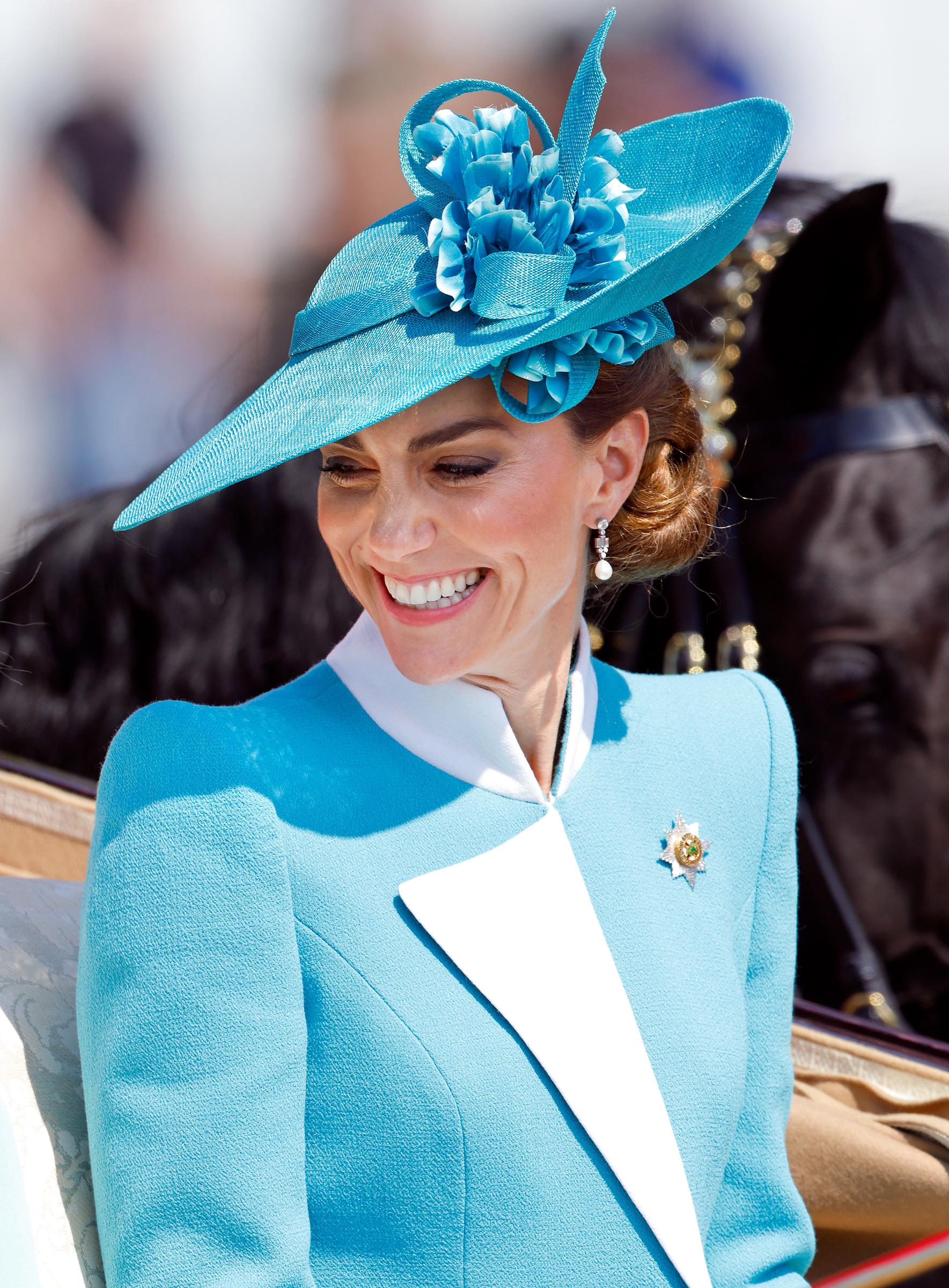 In einer Nahaufnahme, die während ihrer Ankunft in der Kutsche beim Trooping the Colour 2025 aufgenommen wurde, lächelt Prinzessin Catherine die versammelte Menge warmherzig an. Ihr Gesichtsausdruck strahlt ruhige Zuversicht aus, umrahmt von den zarten Blumendetails ihres blaugrünen Hutes und der schlichten Eleganz ihres Ensembles - ein Bild der Anmut, wie sie sich in der Tradition entfaltet.