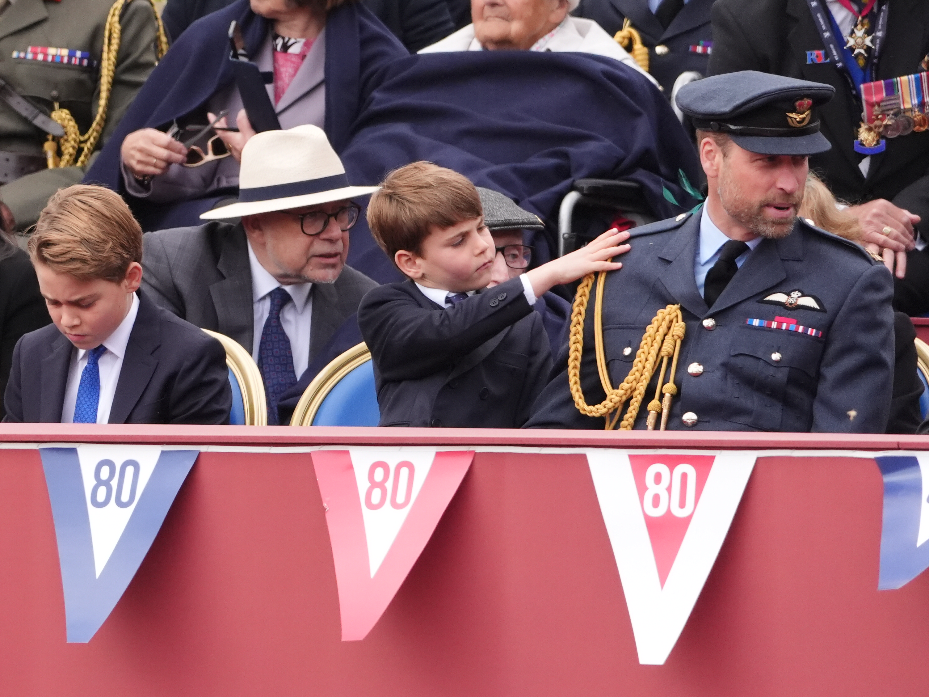 Prinz Louis streift Prinz William sanft die RAF No.1 Uniform ab, während Prinz George auf der anderen Seite von ihm sitzt, während des 80. Jahrestages des VE Day in London, England am 5. Mai 2025. | Quelle: Getty Images