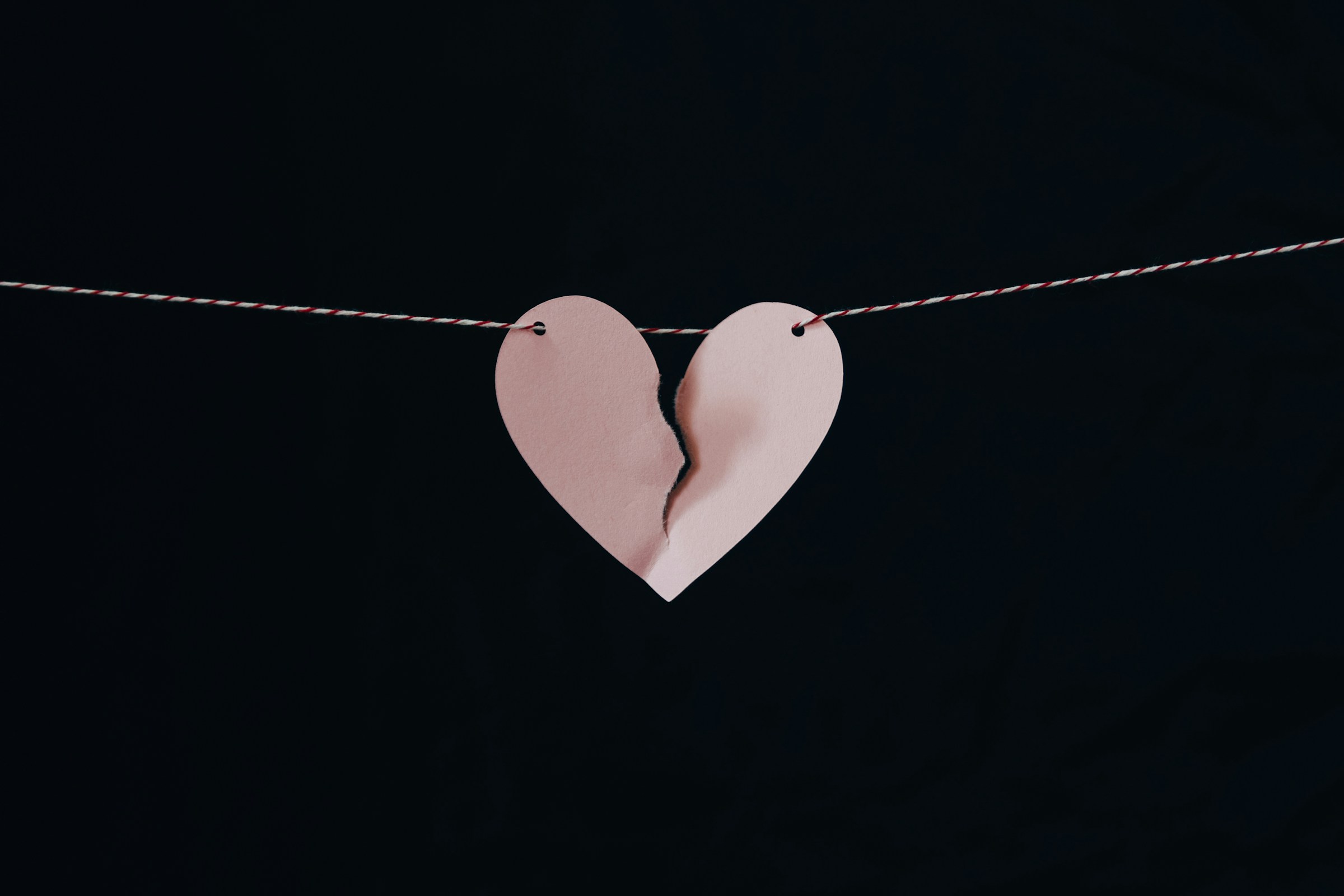 Ein zerbrochenes rosa Papierherz, das an einem Draht hängt | Quelle: Unsplash