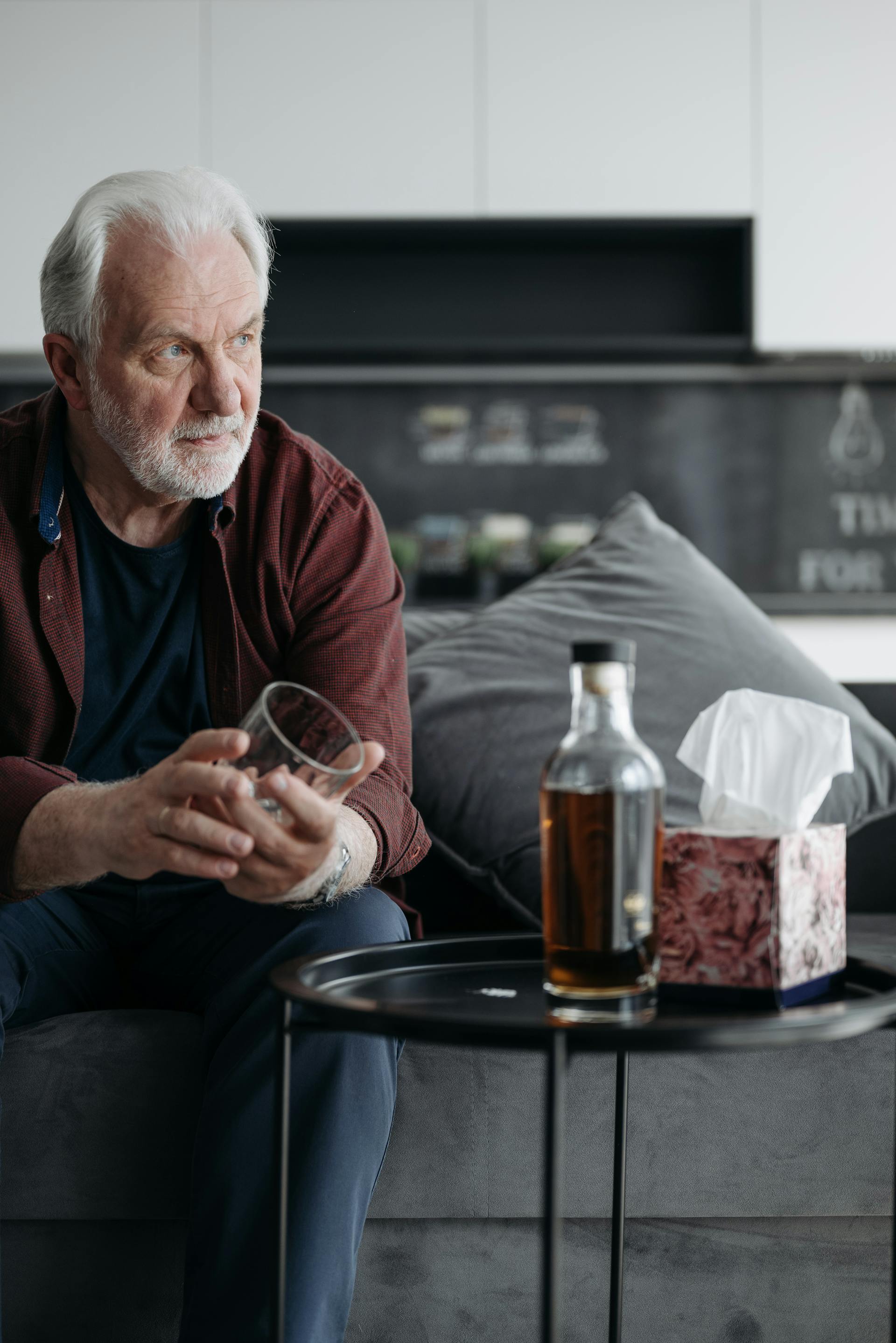 Ein Mann mit einem Glas in der Hand, vor dem eine Bierflasche liegt | Quelle: Pexels