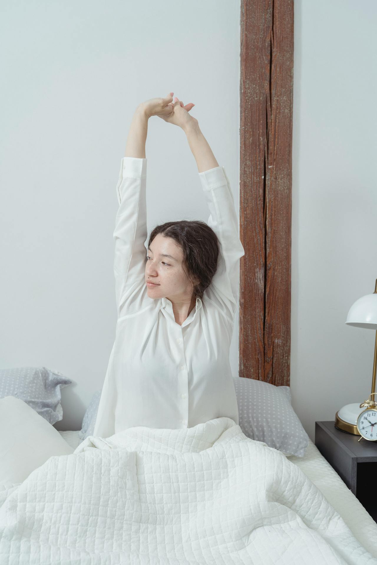 Eine Frau streckt ihre Arme aus, während sie auf dem Bett sitzt | Quelle: Pexels