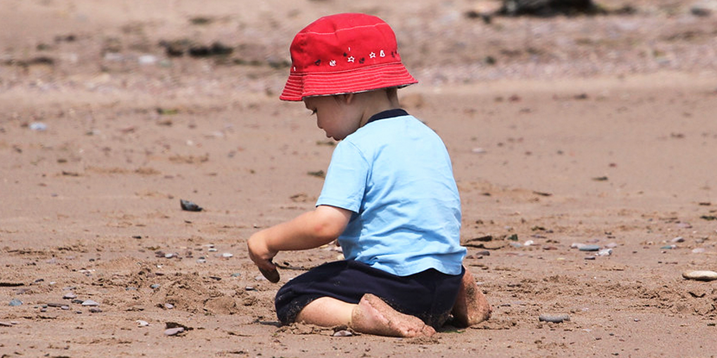 Ein kleiner Junge sitzt auf dem Sand | Quelle: Flickr