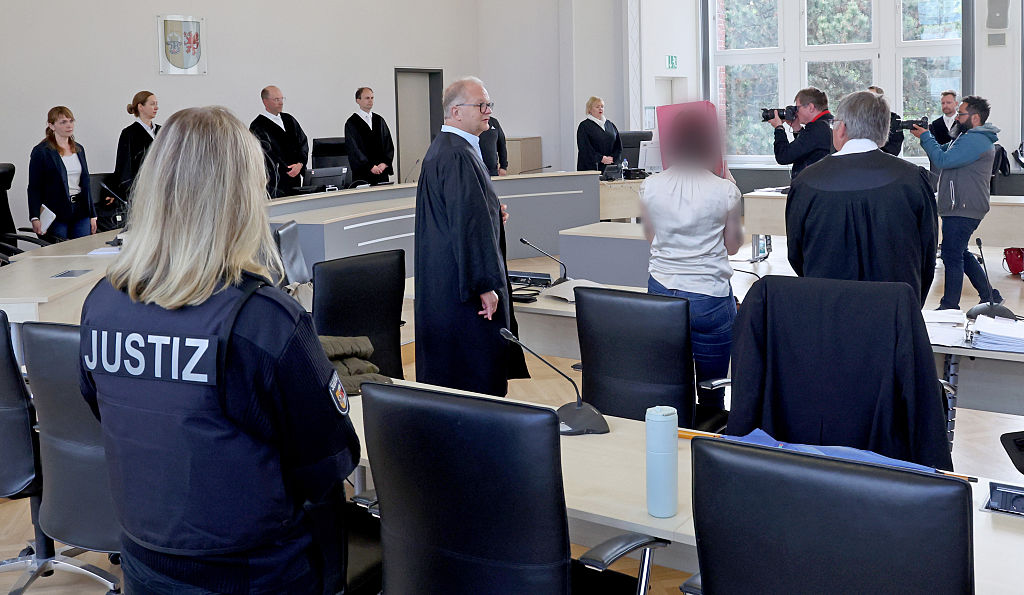 13. Mai 2026, Mecklenburg-Vorpommern, Rostock: Ein Gerichtsangestellter (v. l. n. r.), Rechtsanwalt Thomas Löcker, der Angeklagte und Rechtsanwalt Andreas Ohm stehen zu Beginn der Fortsetzung des Mordprozesses im Gerichtssaal des Landgerichts. | Quelle: Getty Images