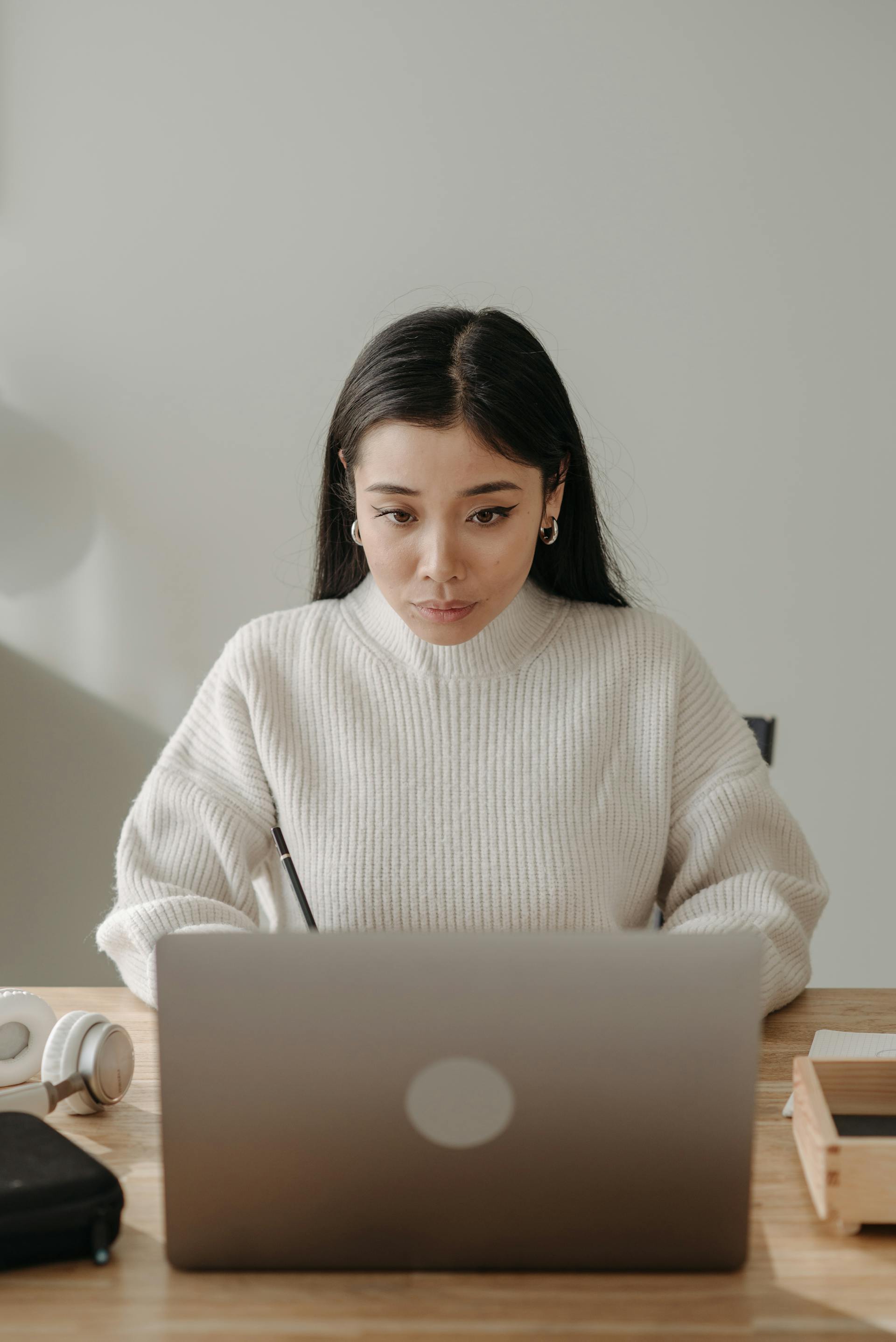 Eine Frau mit dunklen Haaren, die einen weißen Pullover trägt und aufmerksam auf einen Laptop schaut | Quelle: Pexels