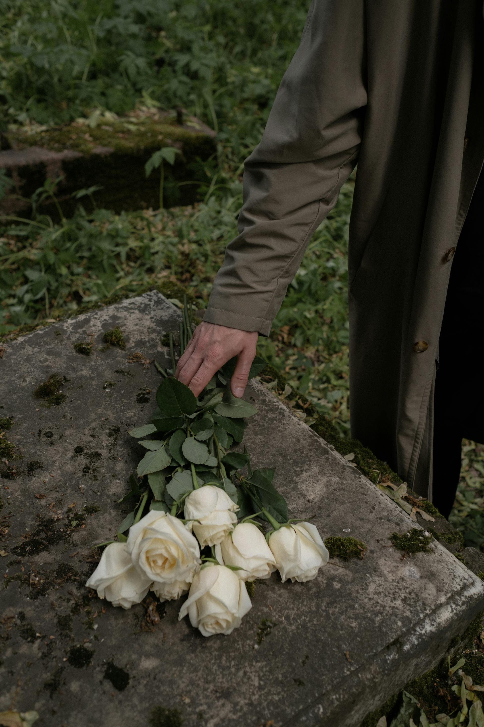 Ein Mann legt weiße Rosen auf eine Betonfläche | Quelle: Pexels