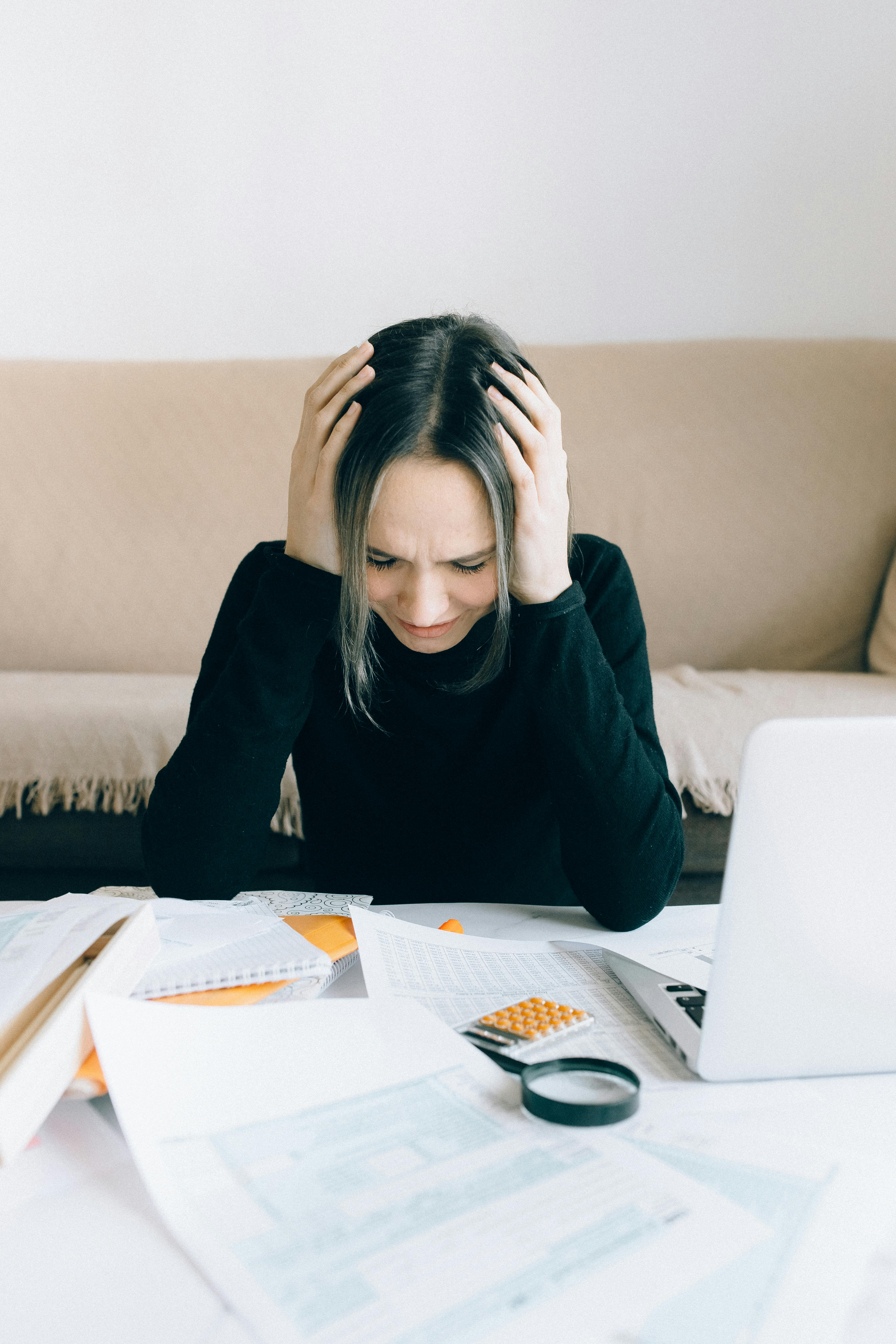 Eine Frau, die an einem Tisch sitzt und sich den Kopf hält | Quelle: Pexels