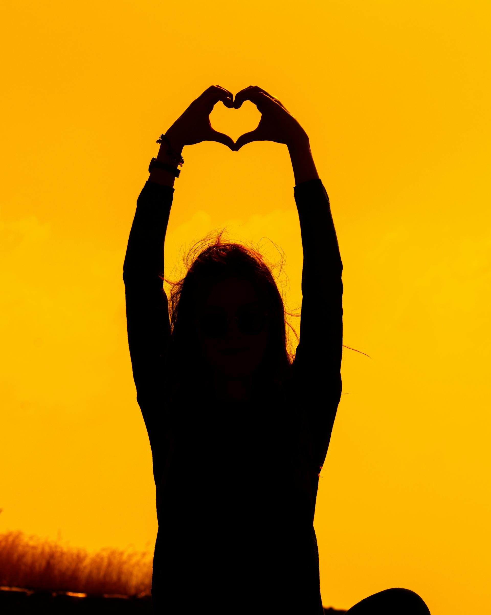 Die Silhouette einer Frau, die bei Sonnenuntergang mit ihren Händen eine Herzform bildet | Quelle: Pexels