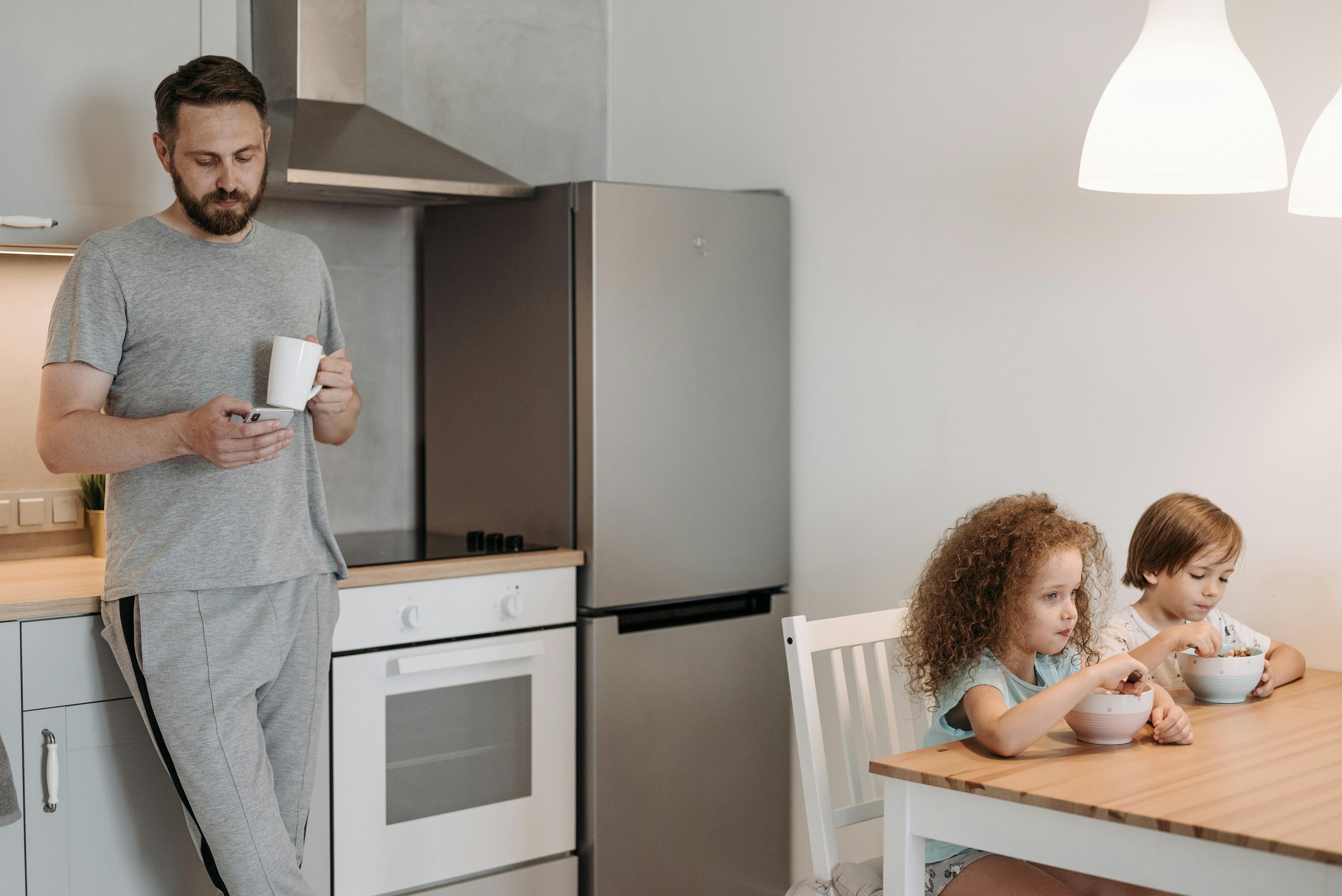 Ein Mann benutzt sein Telefon, während seine Kinder essen | Quelle: Pexels