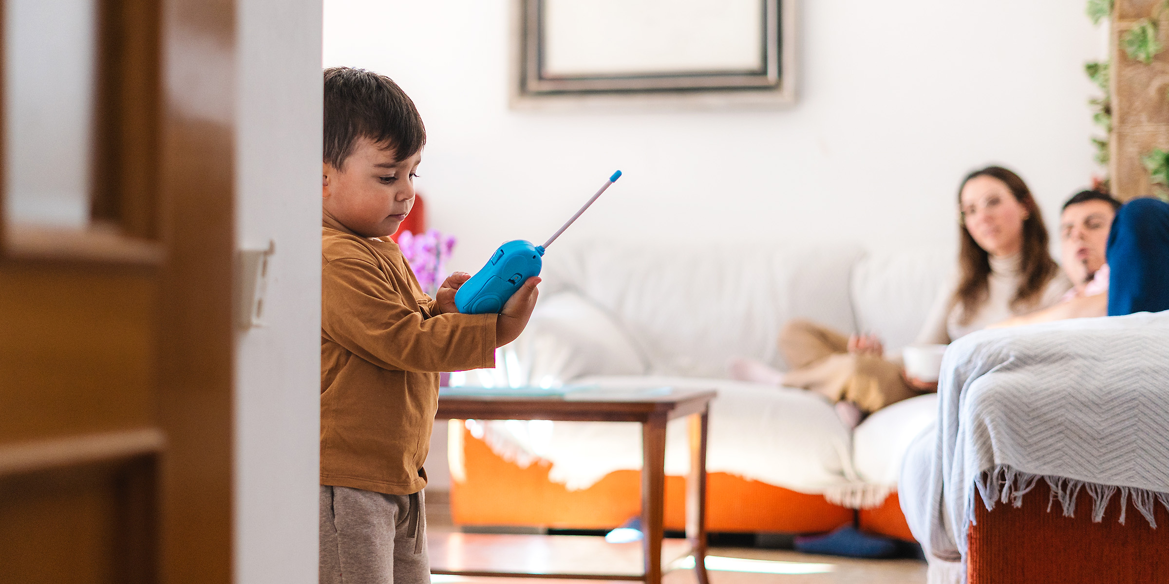 Ein kleiner Junge spielt mit einem blauen Walkie-Talkie, während zwei Erwachsene von der Couch aus zusehen | Quelle: Shutterstock