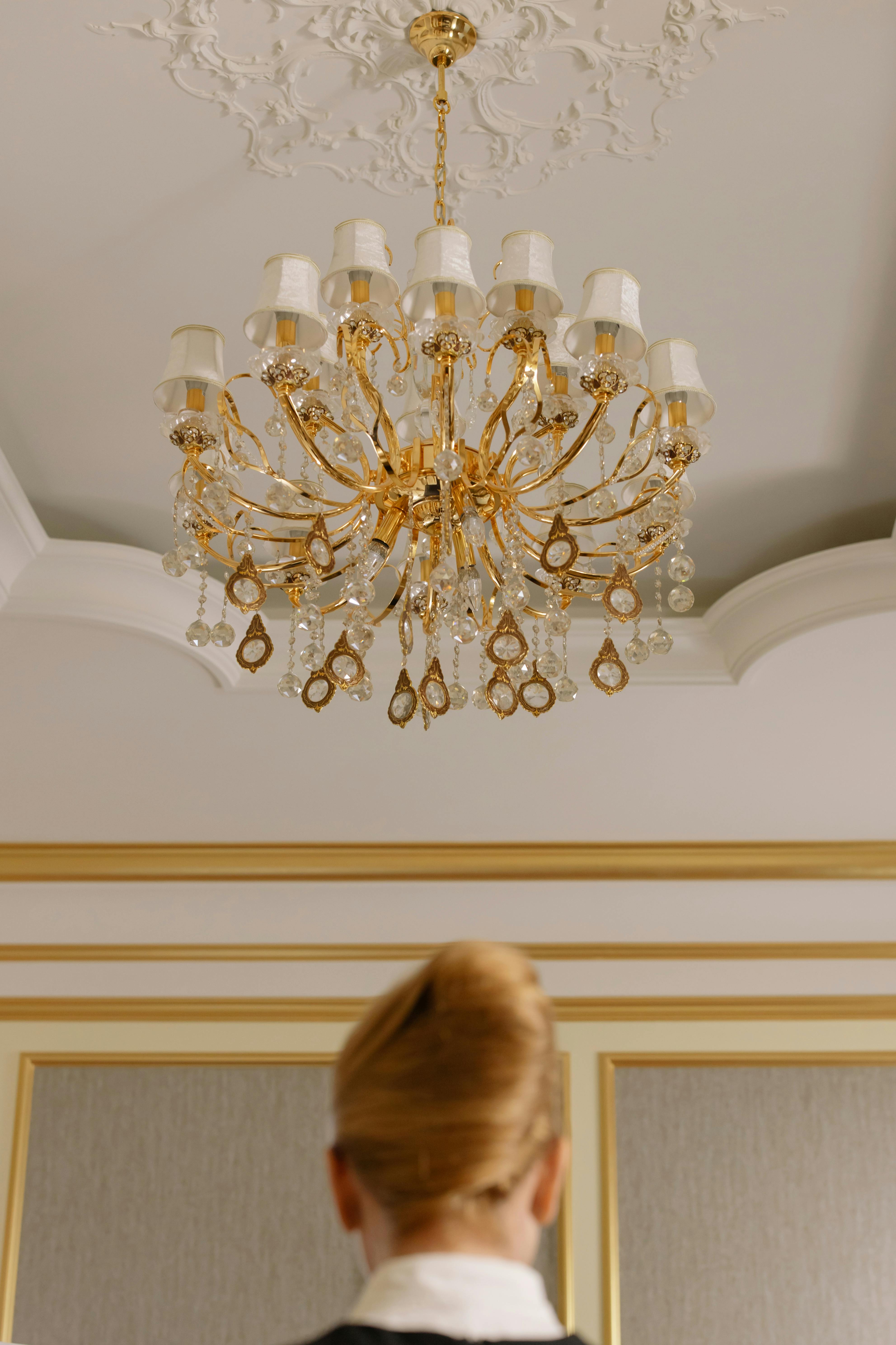 Frau steht unter einem Kronleuchter in einem Hotelzimmer | Quelle: Pexels