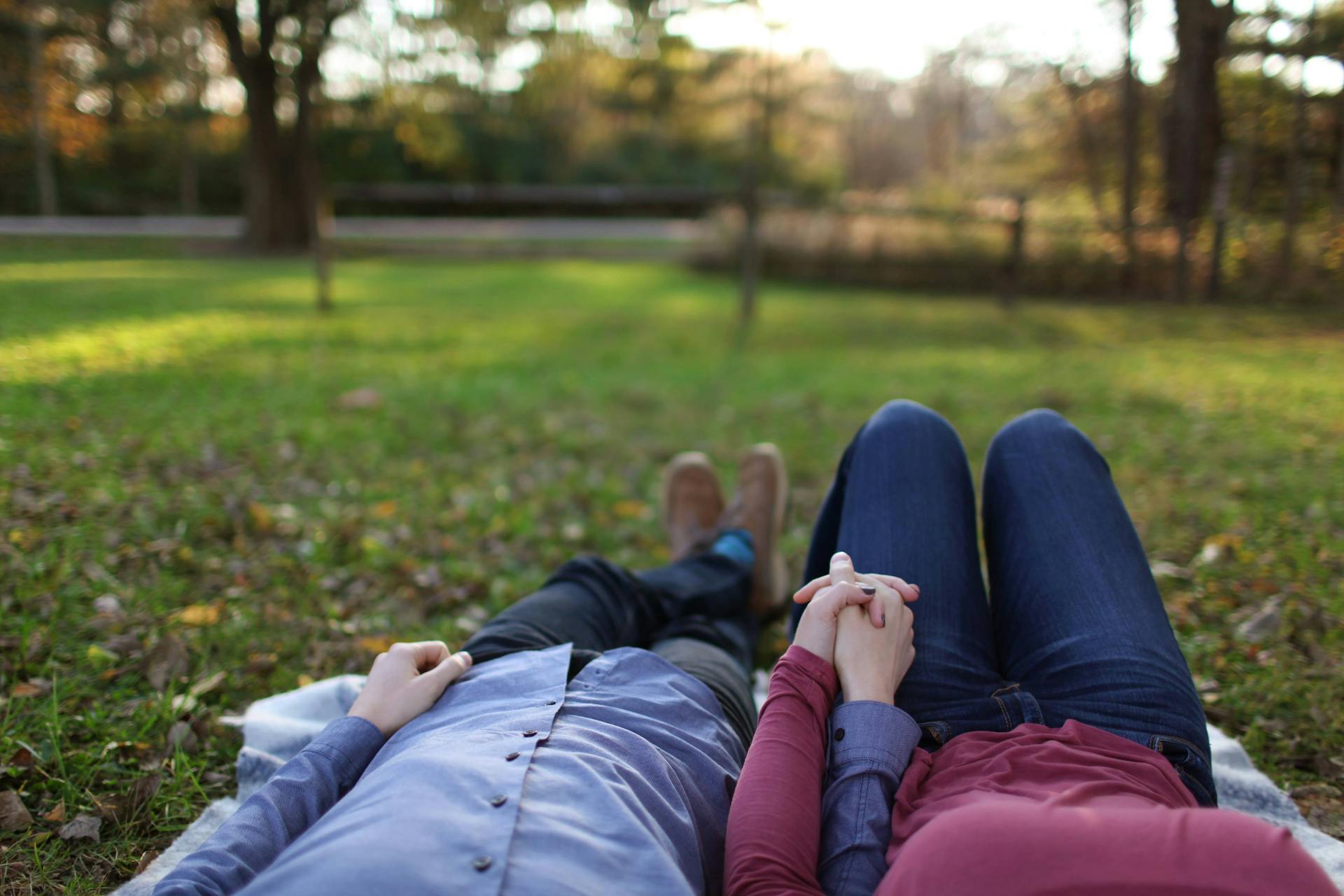 Ein Paar liegt im Gras und hält sich an den Händen | Quelle: Pexels