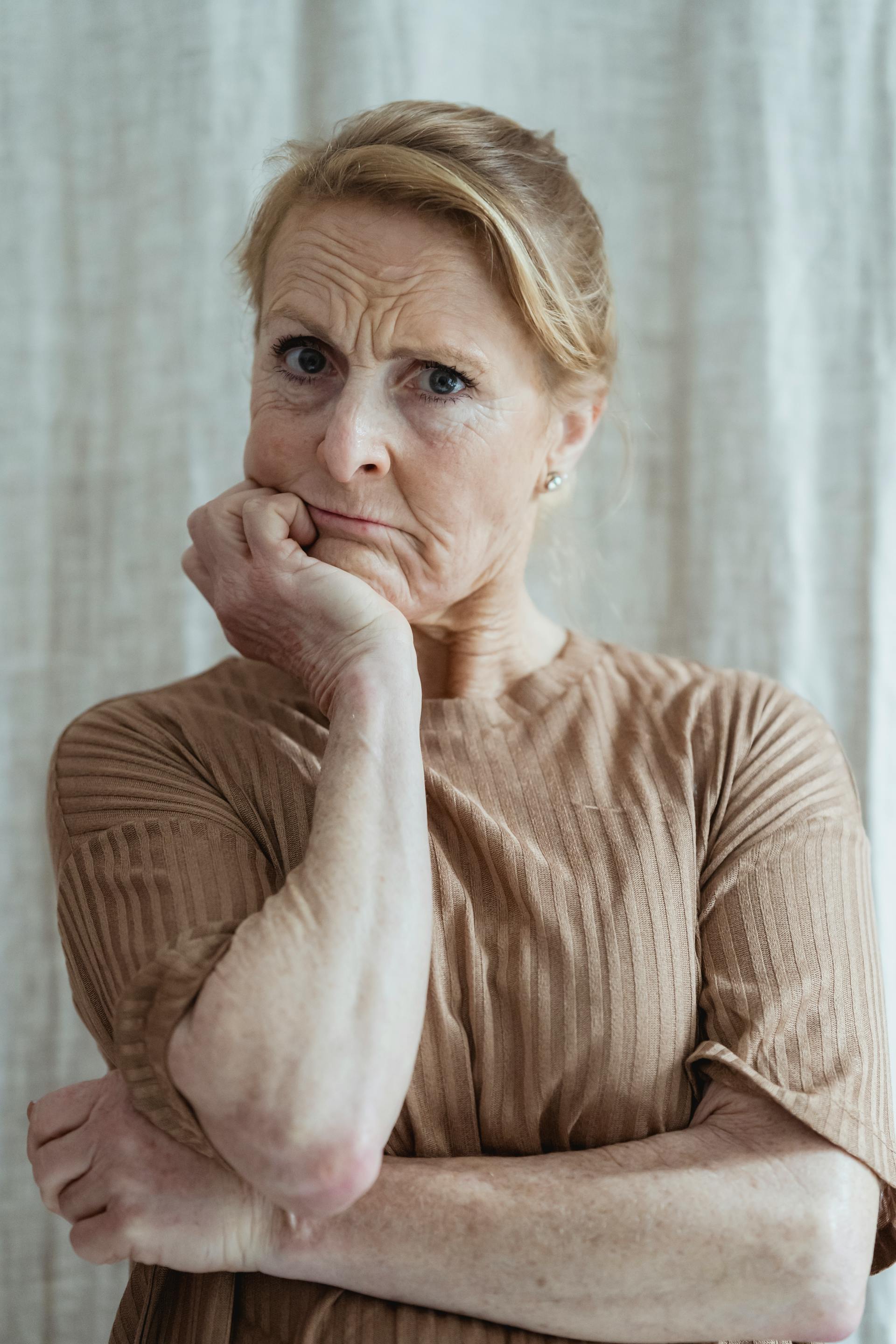 Eine besorgte reife Frau in einem braunen Pullover mit der Hand am Kinn, die nach vorne schaut | Quelle: Pexels