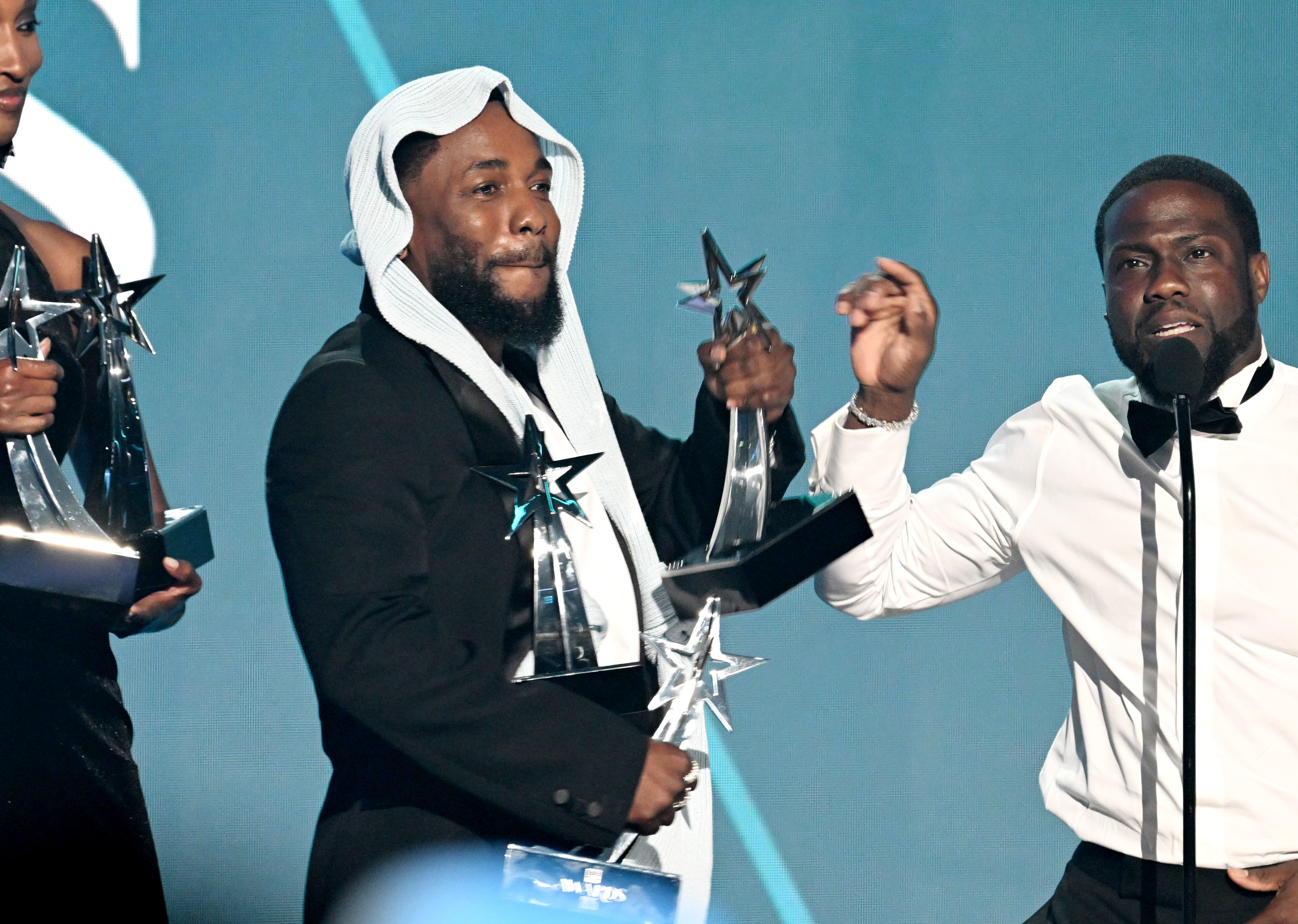 Kendrick Lamar steht neben Comedian Kevin Hart und jongliert mit mehreren seiner fünf BET Awards-Trophäen. Der humorvolle Austausch folgte auf Lamars emotionale Rede und fand live auf der Bühne der BET Awards 2025 in Los Angeles statt.