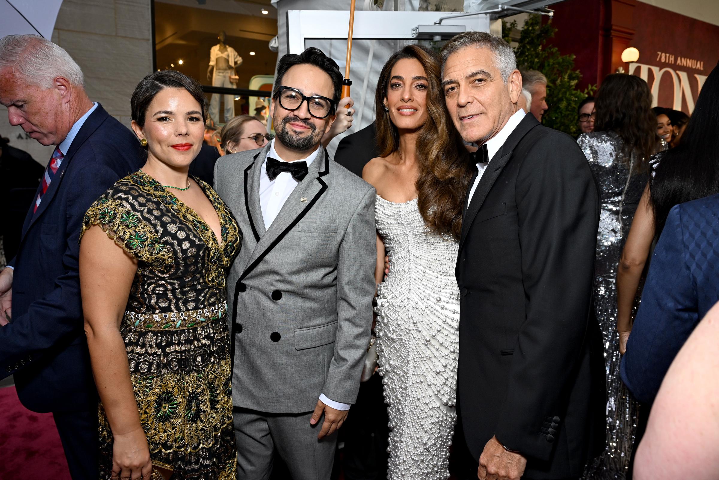 George und Amal Clooney stellen sich mit Lin-Manuel Miranda und Vanessa Nadal für ein Gruppenfoto bei den Tony Awards auf. Amals perlenbesetztes Kleid verleiht dem freundschaftlichen Moment einen besonderen Glanz, während George sich mit einem gelassenen halben Lächeln zurücklehnt.