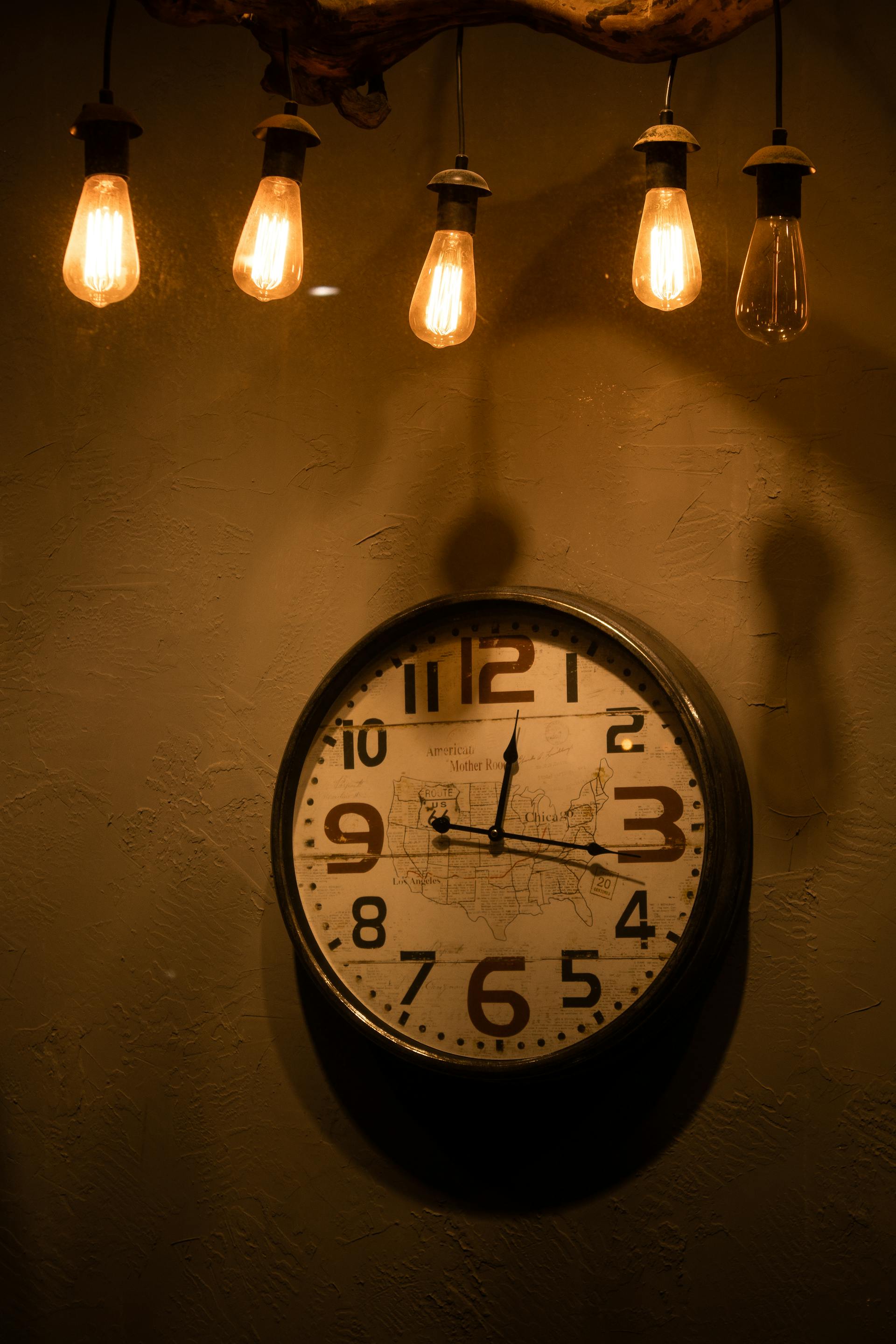 Glühbirnen hängen über einer analogen Uhr | Quelle: Pexels