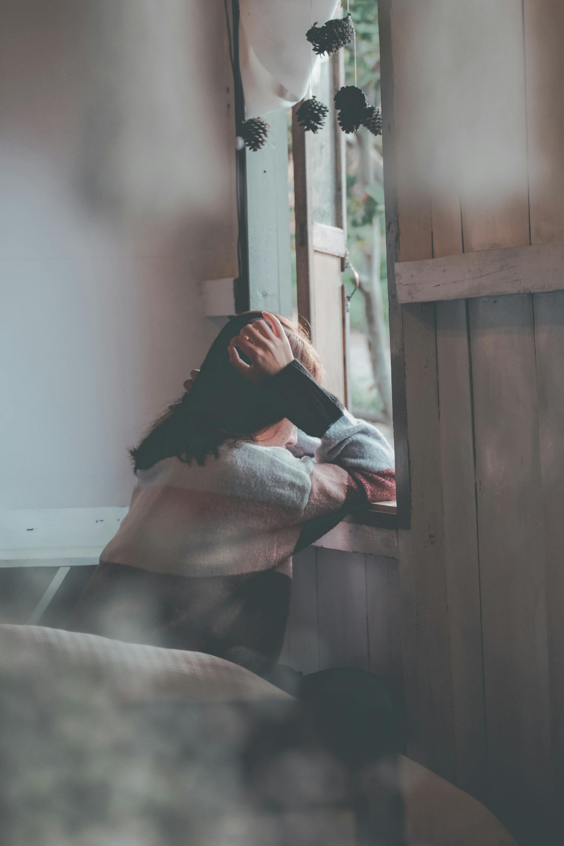 Eine Rückansicht einer Frau, die sich an ein Holzfenster lehnt | Quelle: Pexels