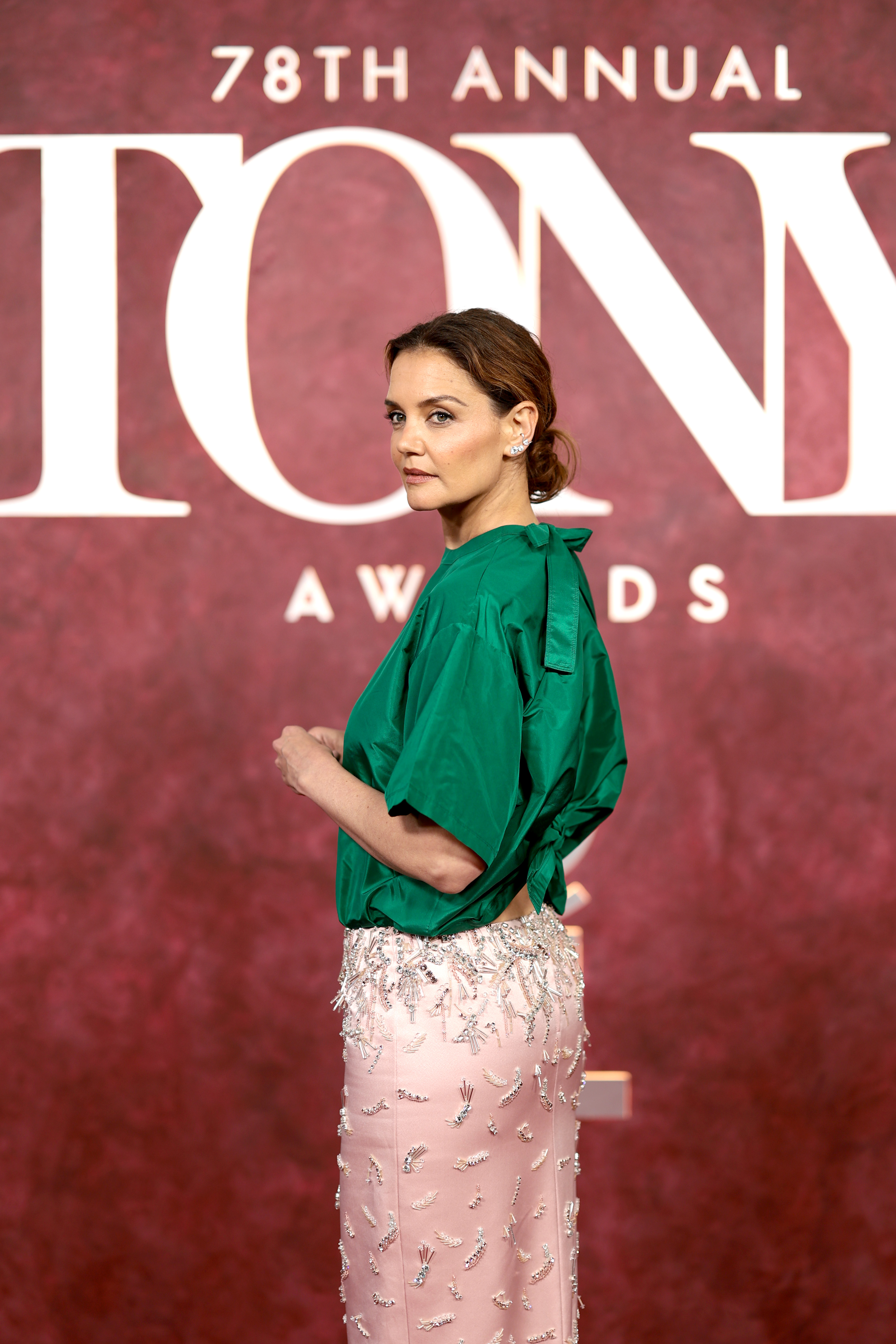 Vor der kultigen Kulisse der Tony Awards hält Katie Holmes im Profil inne. Ihr gewagter zweifarbiger Look – oben satingrün, unten rosafarben und mit silbernen Perlen besetzt – zieht die Aufmerksamkeit von Modebeobachtern und Fotografen gleichermaßen auf sich.
