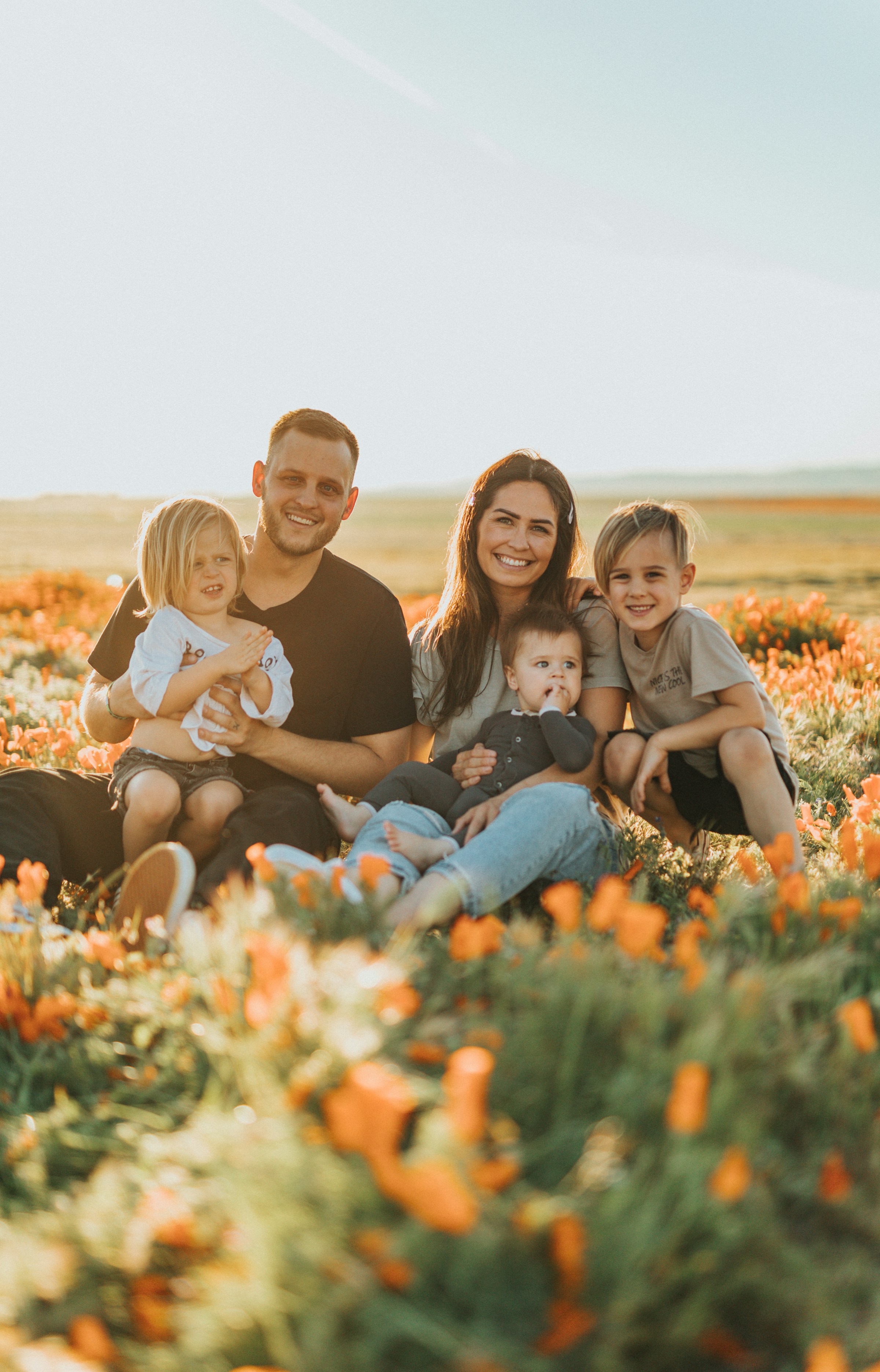 Ein glückliches Paar mit seinen drei Kindern, die zusammen auf einer Wiese sitzen | Quelle: Unsplash