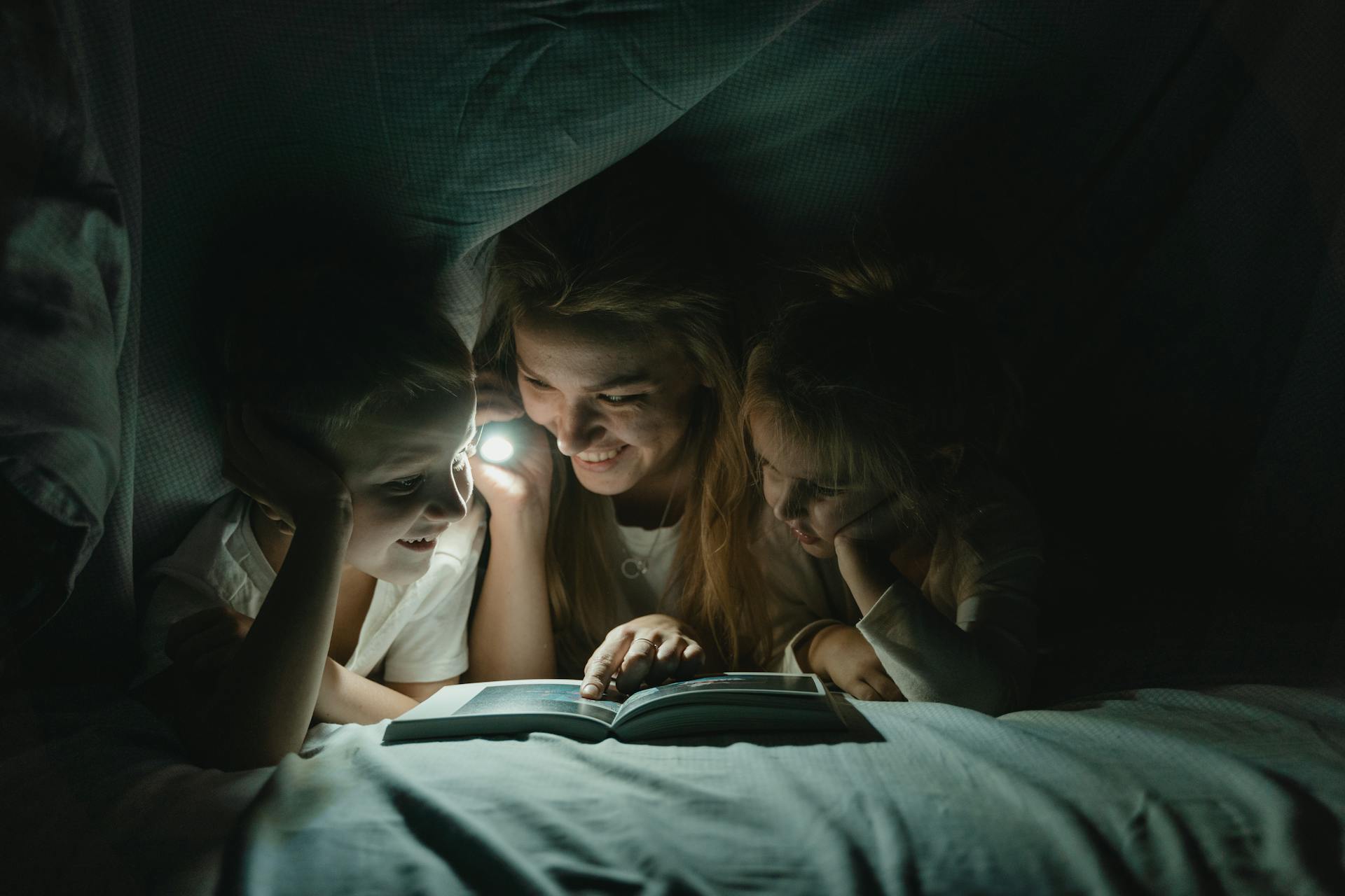 Eine Frau hält eine Taschenlampe und liest ihren Kindern eine Geschichte vor | Quelle: Pexels