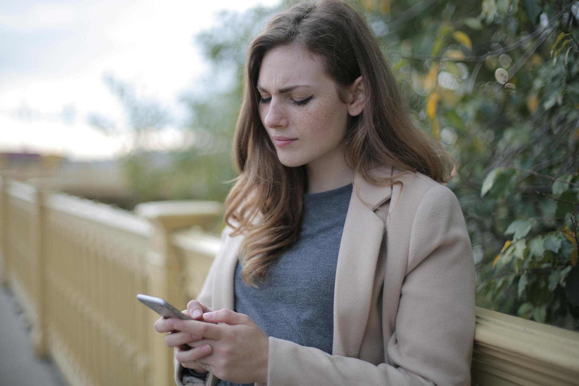 Eine Frau, die die Stirn runzelt, während sie auf ihr Telefon schaut | Quelle: Pexels