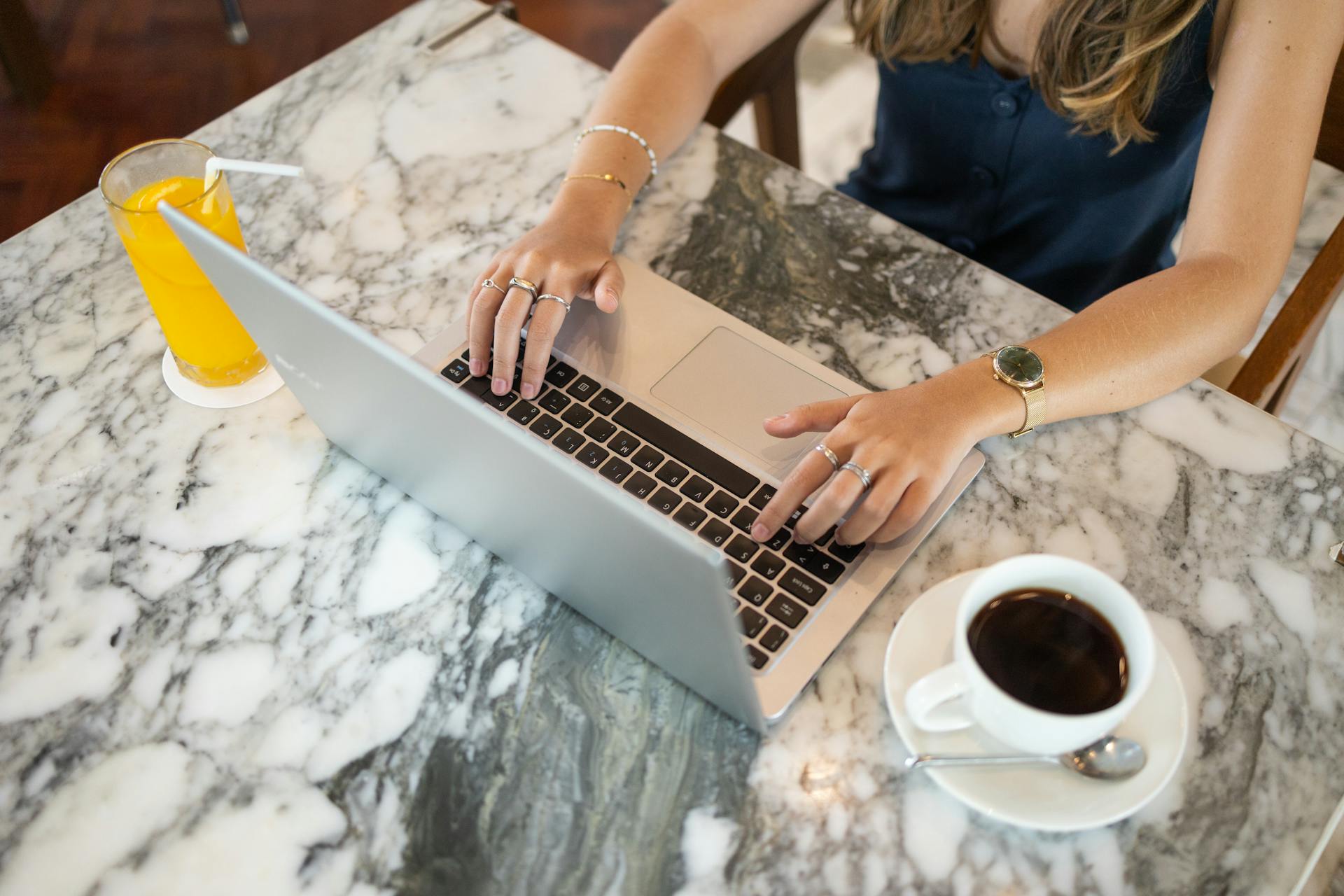 Eine Frau, die an ihrem Laptop arbeitet und eine Tasse Kaffee und Saft vor sich auf dem Tisch stehen hat | Quelle: Pexels
