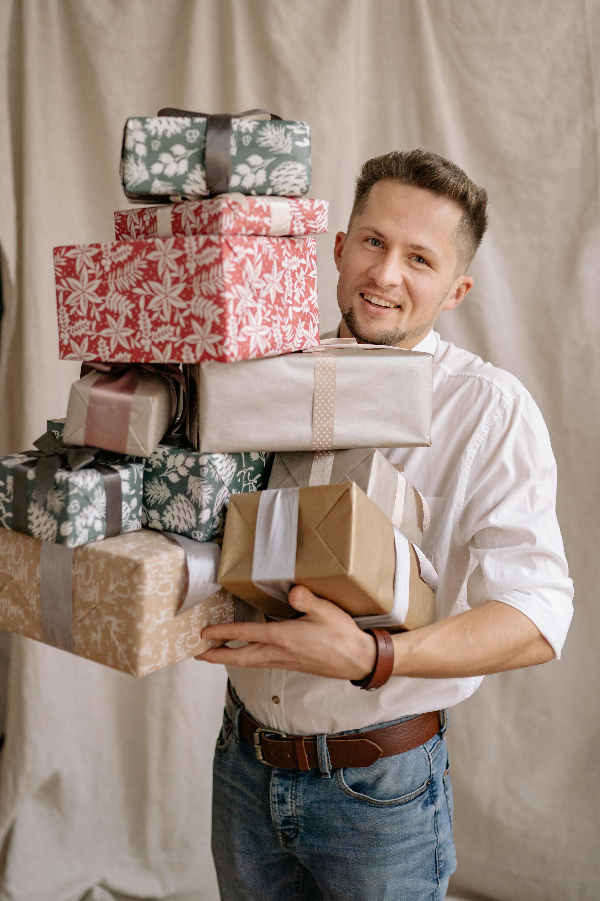 Ein Mann in weißem Hemd und Jeans hält einen großen Stapel eingepackter Geschenke | Quelle: Pexels