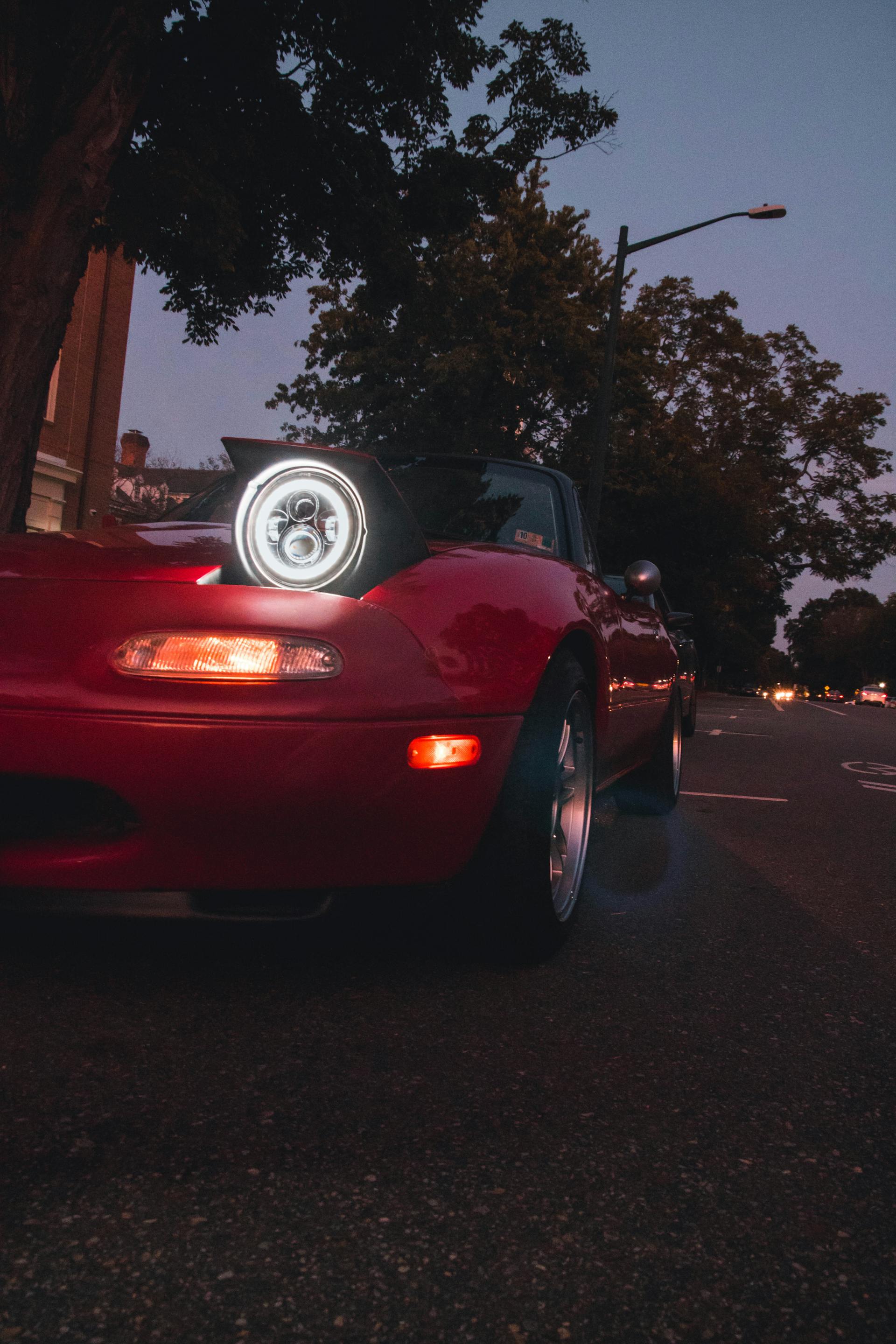 Ein rotes Auto mit eingeschalteten Scheinwerfern bei Nacht | Quelle: Pexels