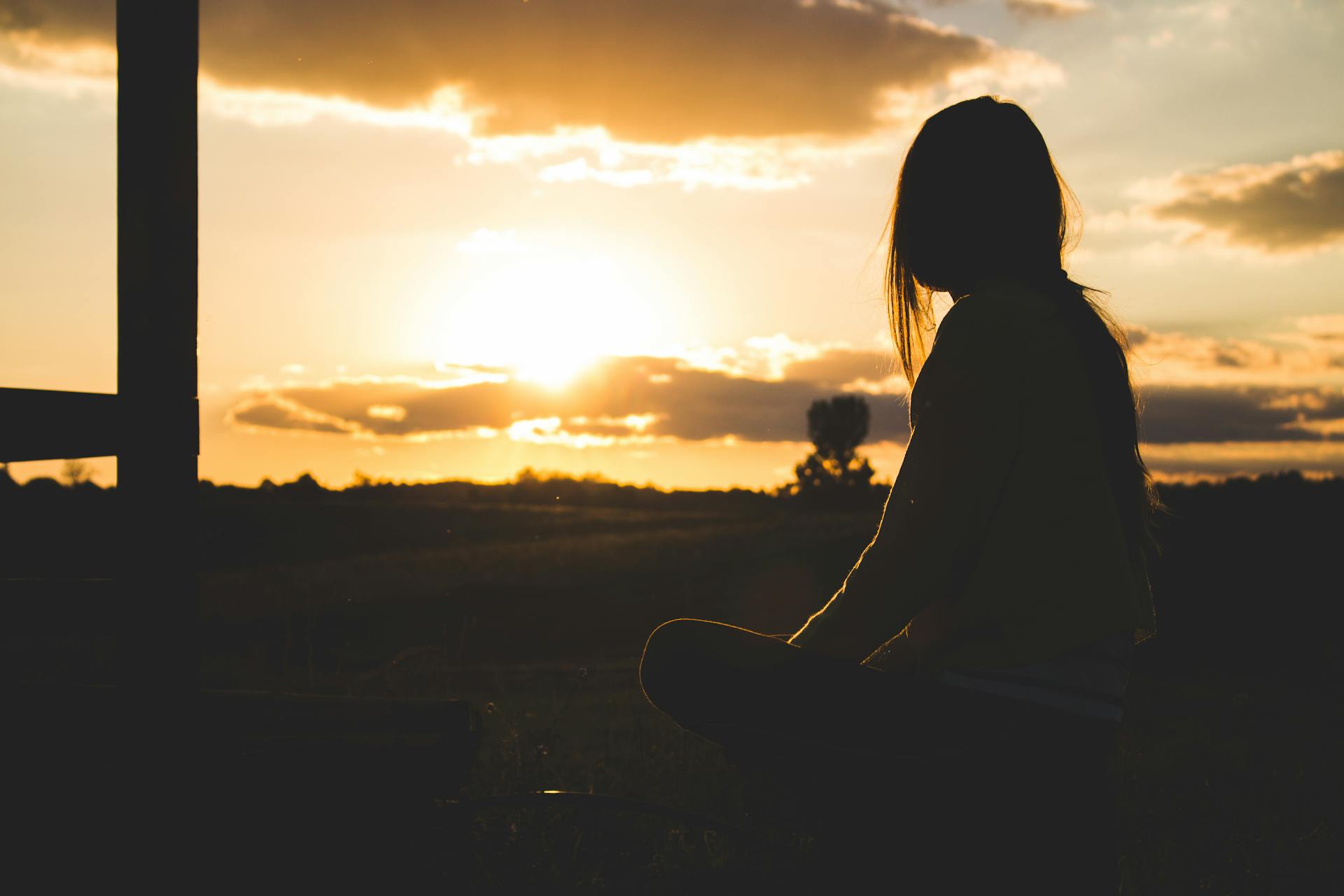 Silhouette einer Frau, die während der goldenen Stunde draußen sitzt | Quelle: Pexels