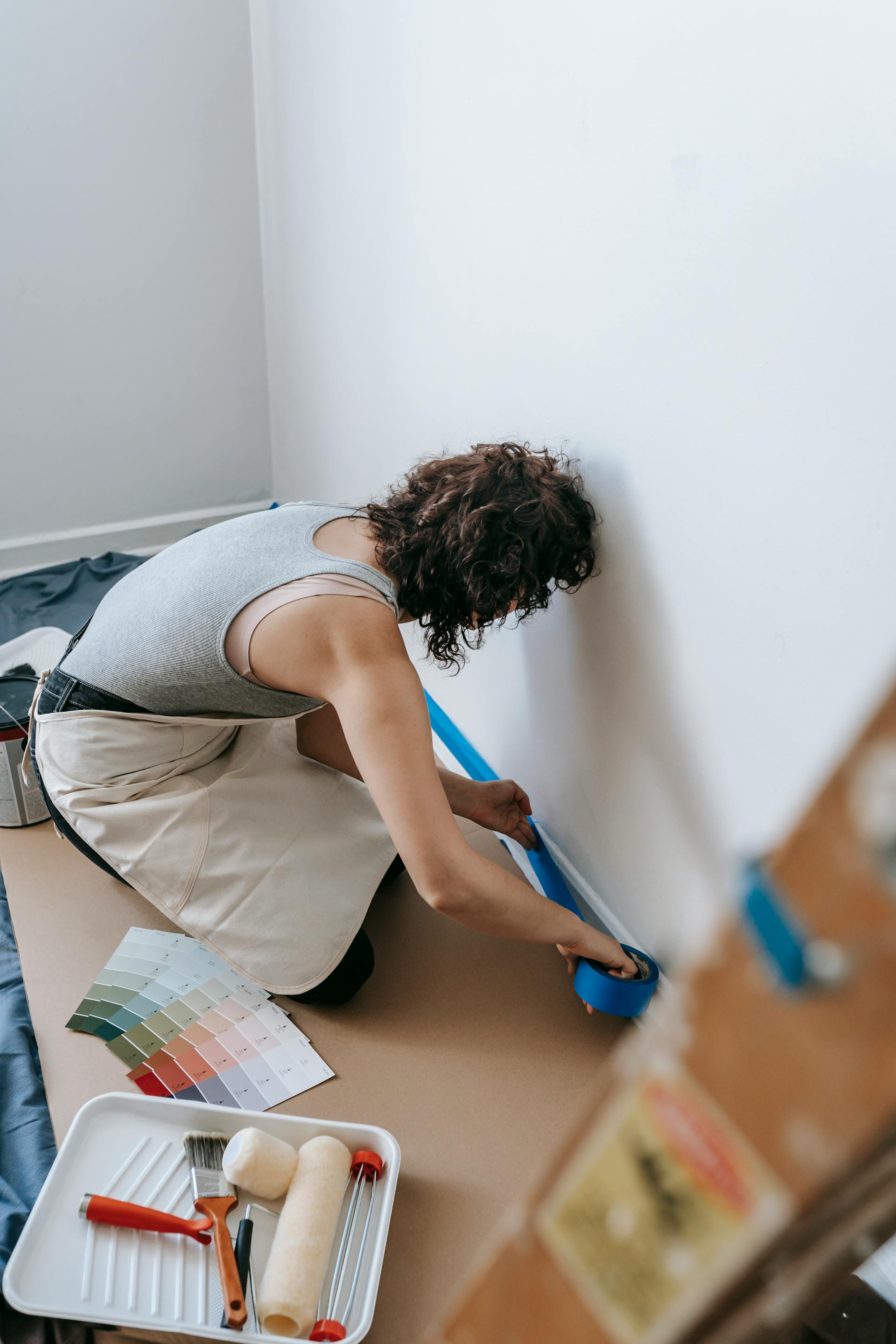 Eine Frau, die sich auf das Streichen vorbereitet, indem sie die Wand abklebt | Quelle: Pexels