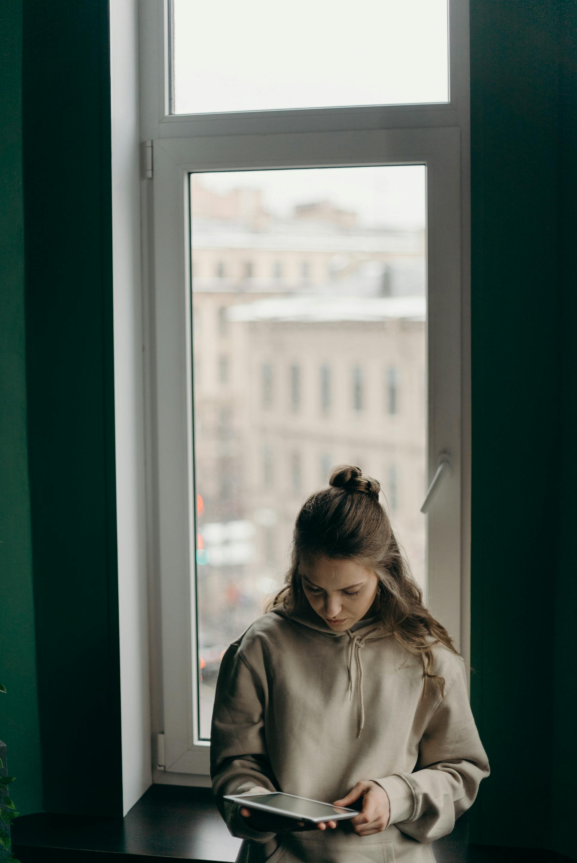 Eine Frau schaut auf ihr iPad, während sie am Fenster steht | Quelle: Pexels