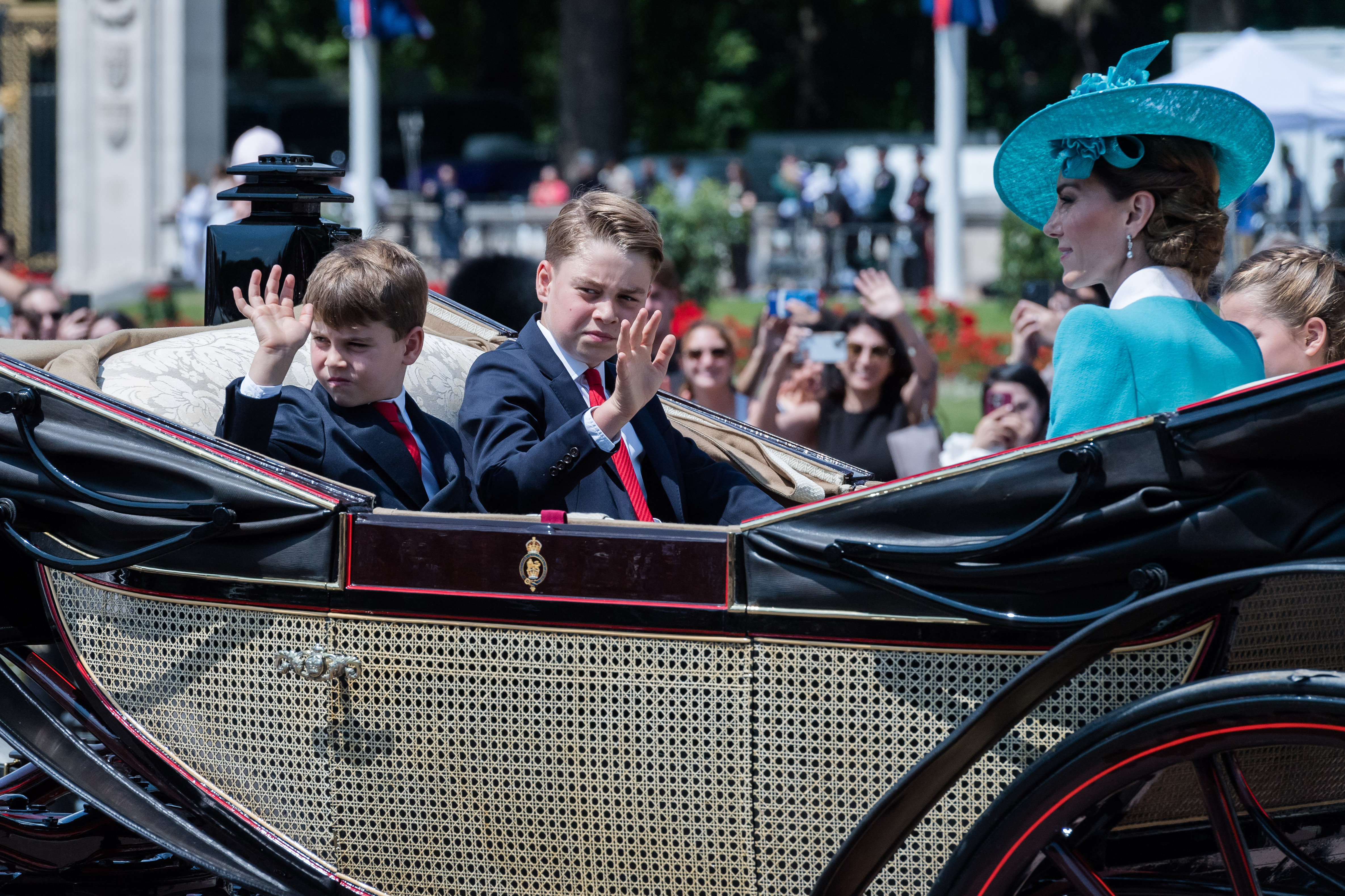 Prinz Louis und Prinz George winken der Menge zu, während Prinzessin Catherine lächelt und Prinzessin Charlotte neben ihr sitzt. | Quelle: Getty Images