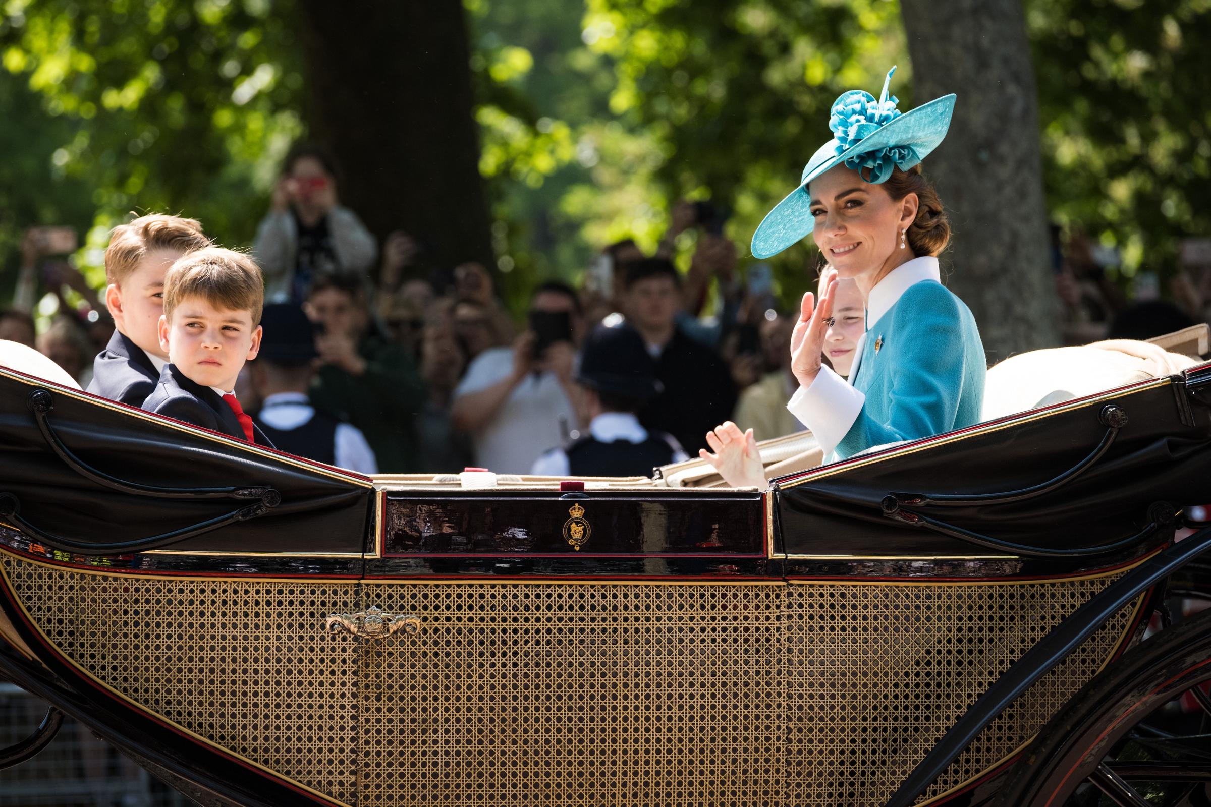 Prinzessin Charlotte, Prinzessin Catherine, Prinz George und Prinz Louis fahren in der königlichen Kutsche, während Catherine und Prinzessin Charlotte dem Volk zuwinken.