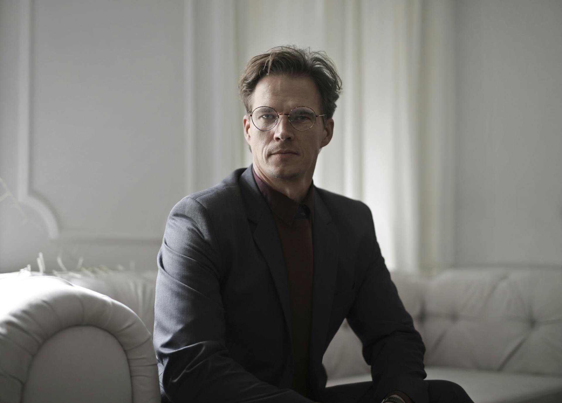 Ein Mann mit Blazer und Brille sitzt auf einem Sofa | Quelle: Pexels
