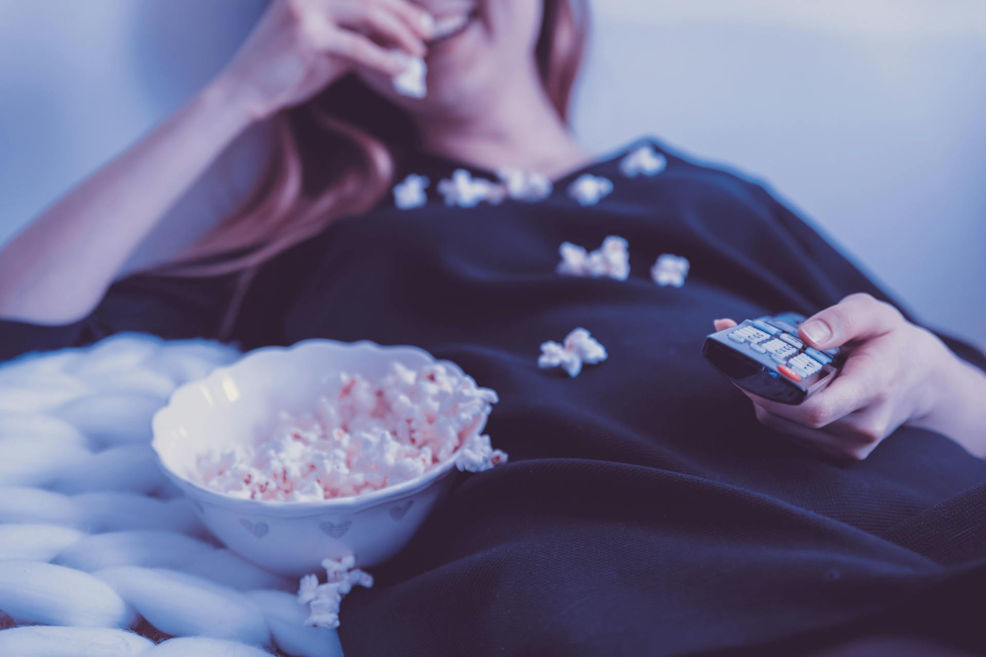 Eine Frau isst Popcorn, während sie eine TV-Fernbedienung hält | Quelle: Pexels