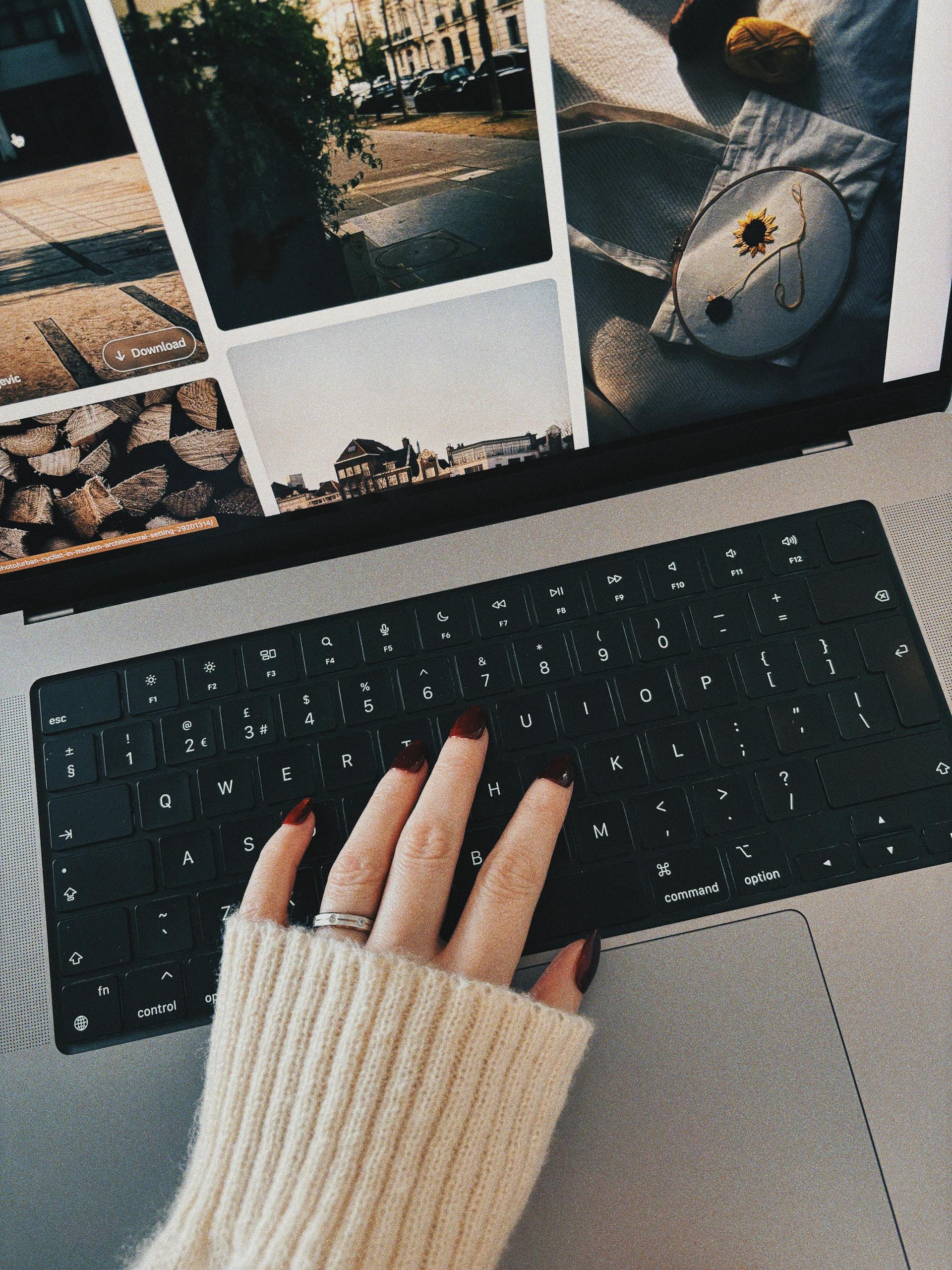 Eine Person mit rot-manikürten Nägeln und einem weißen Pullover an ihrem Laptop | Quelle: Pexels
