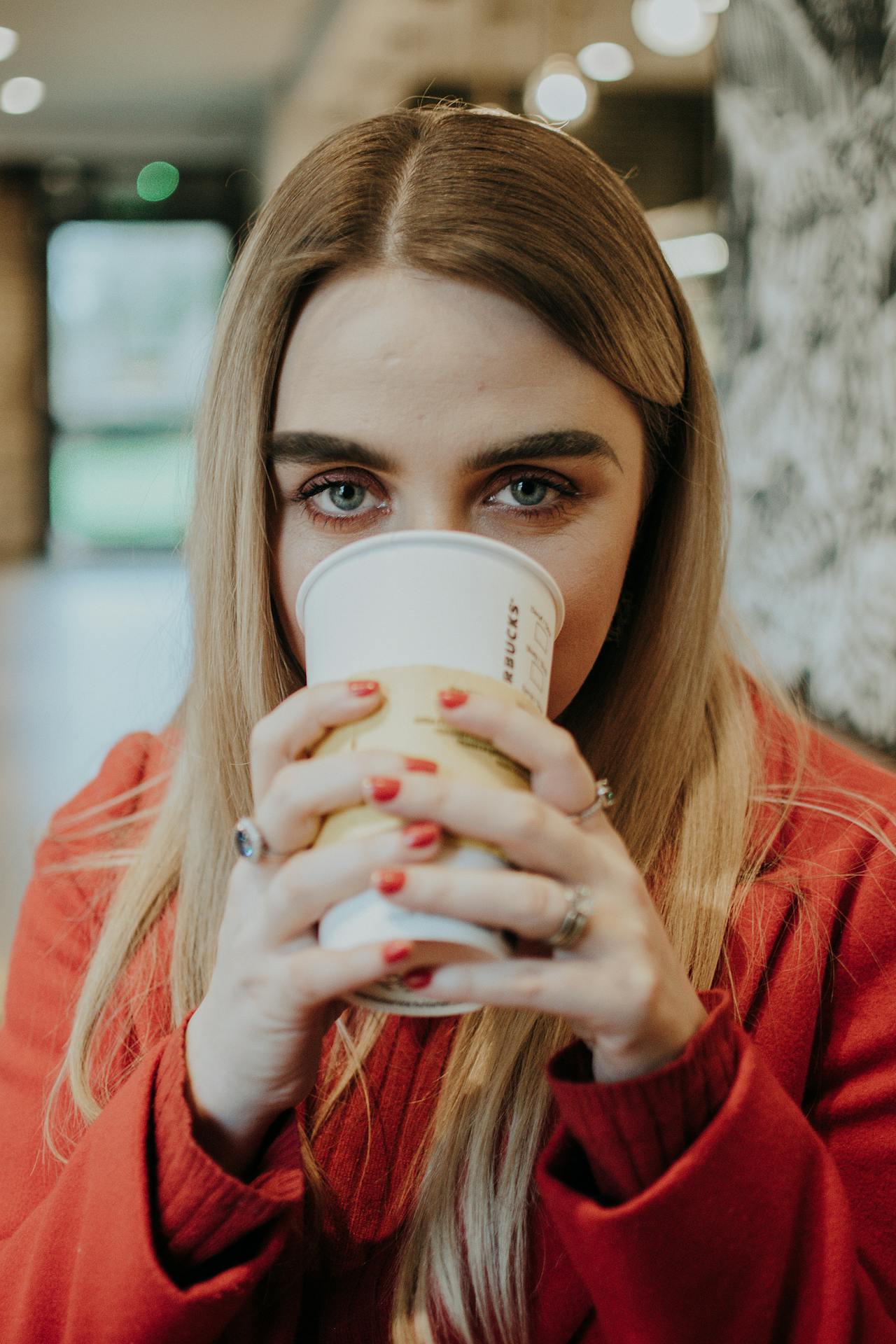 Eine Frau, die aus einem Einwegbecher trinkt und neugierig starrt | Quelle: Pexels
