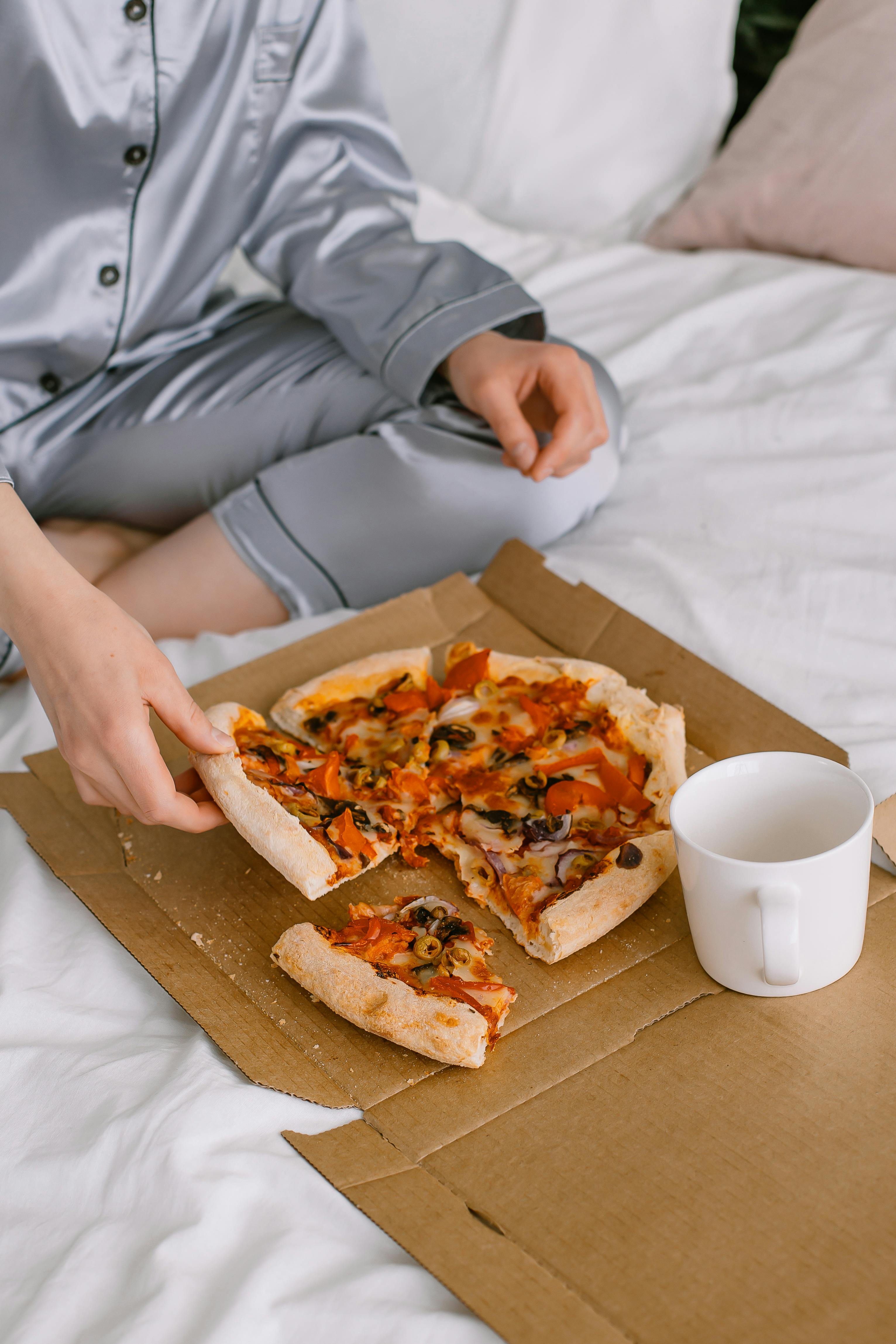 Eine Person, die auf einem Bett mit einer Pizzaschachtel sitzt | Quelle: Pexels