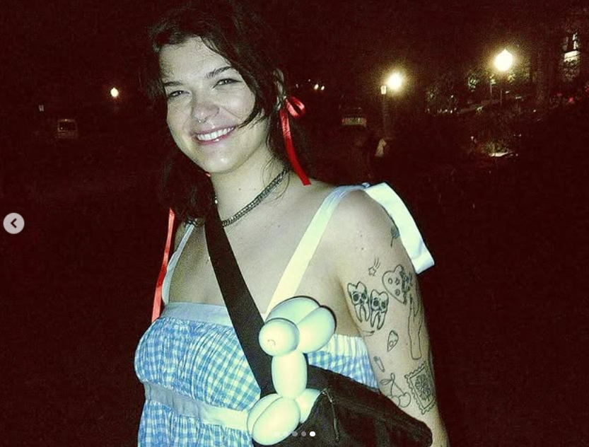 Kendall Fortner lächelt in einem blau-karierten Kleid mit roten Bändern im Haar und einem verspielten Ballontier, das sie an ihrer Tasche befestigt hat | Quelle: Instagram/kendall_fortner