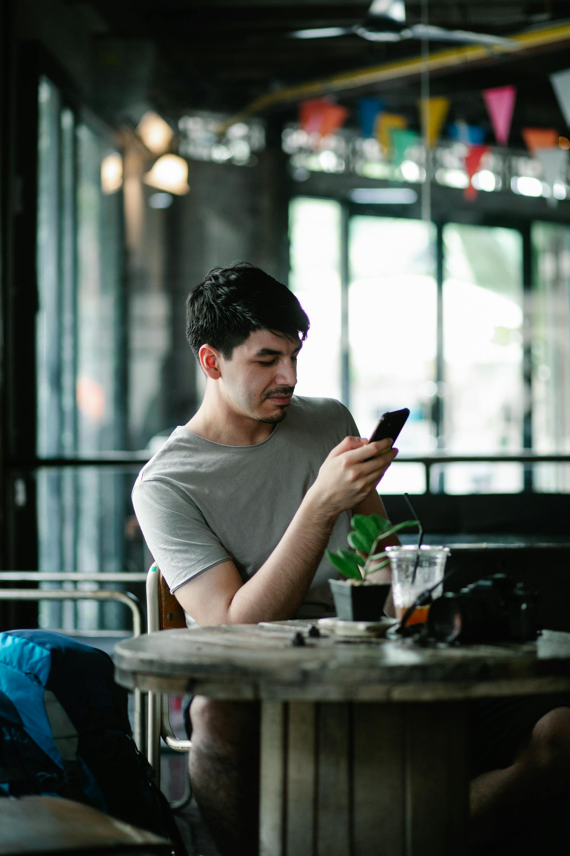 Ein Mann mit dunklen Haaren in einem grauen Hemd sitzt an einem Tisch in einem Café und schaut auf sein Handy | Quelle: Pexels