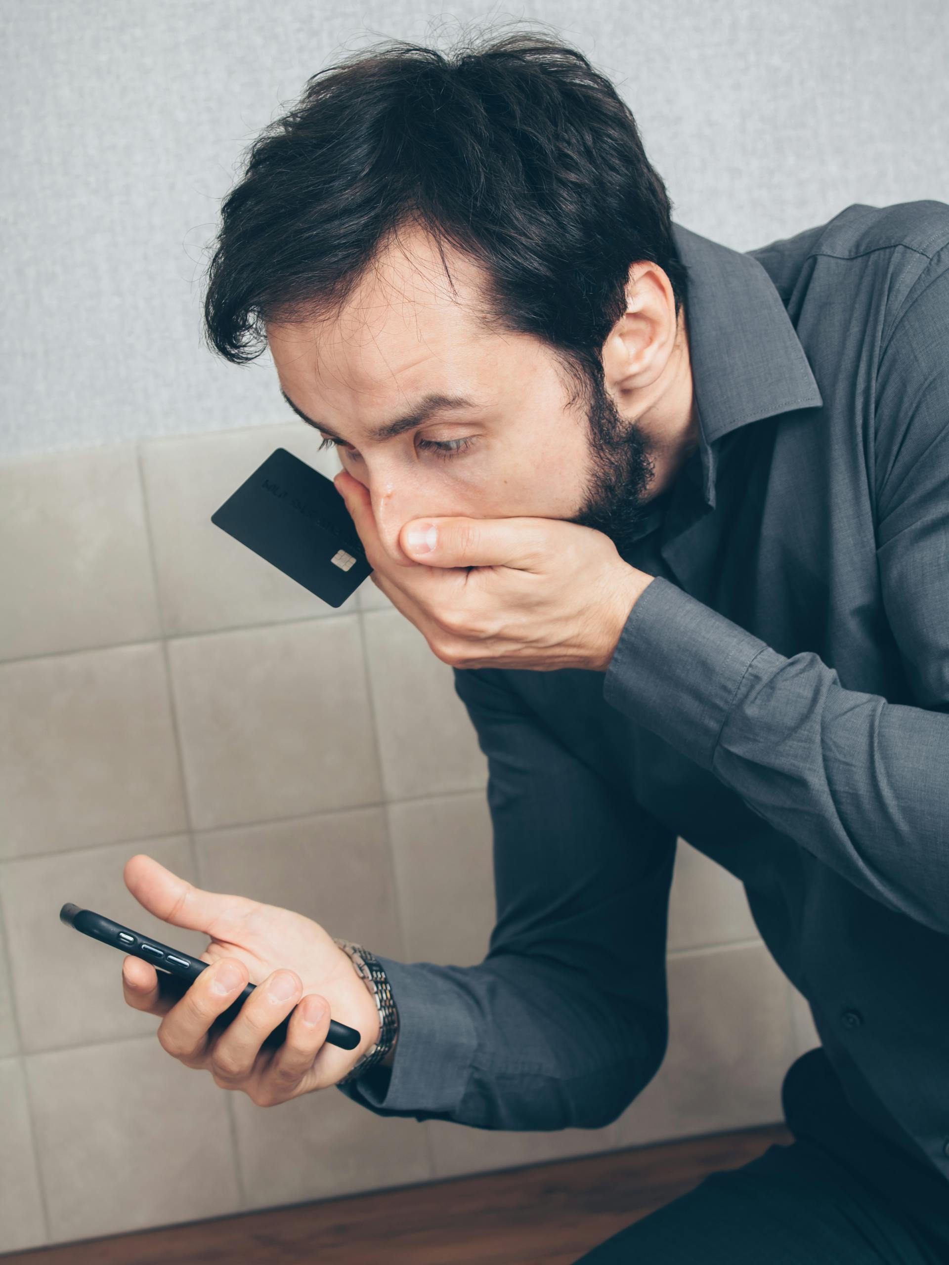 Ein Mann hält eine Kreditkarte in der Hand und starrt schockiert auf sein Handy: Pexels
