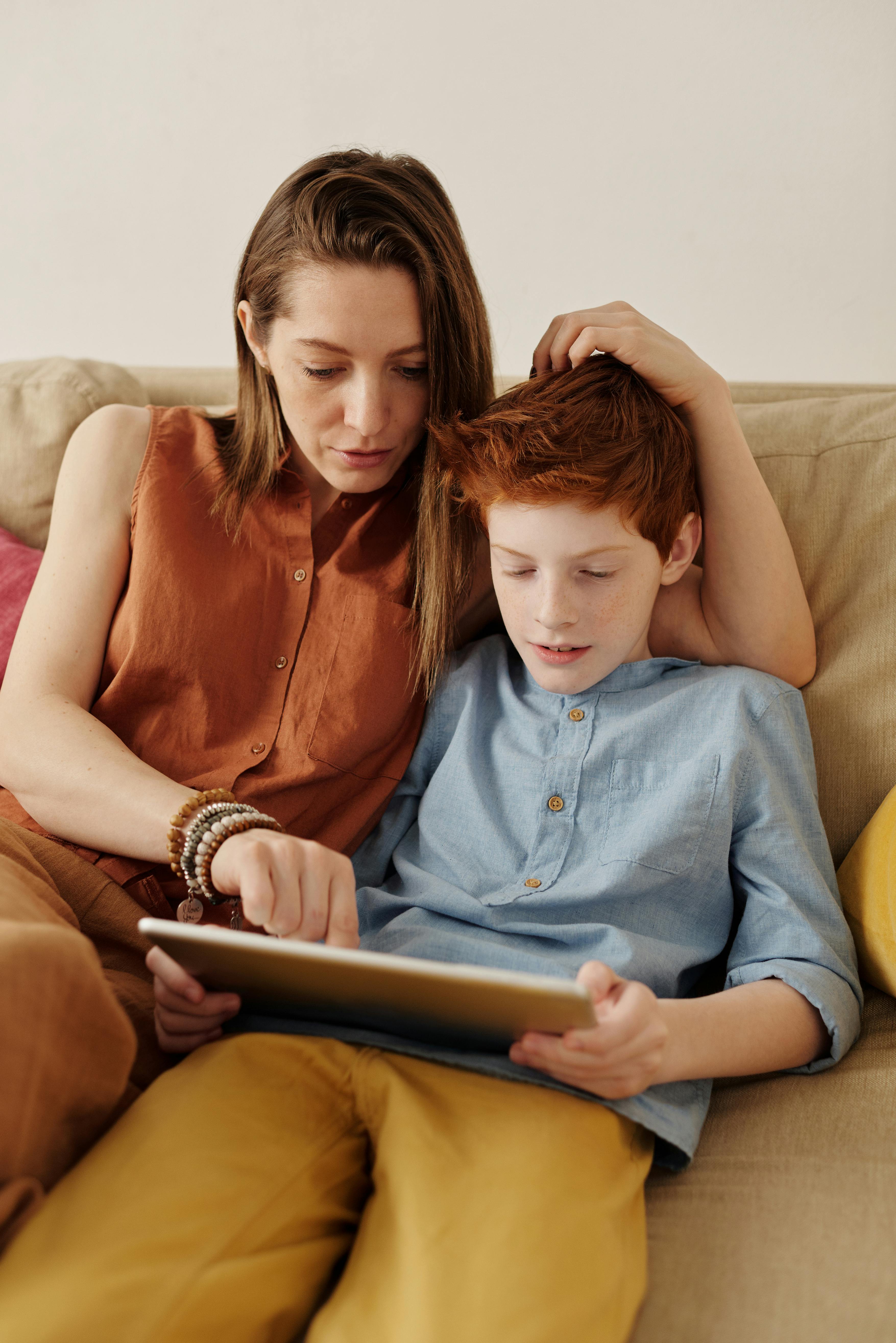 Mutter und ihr Sohn sitzen auf einer Couch und schauen auf ein Tablet | Quelle:  Pexels