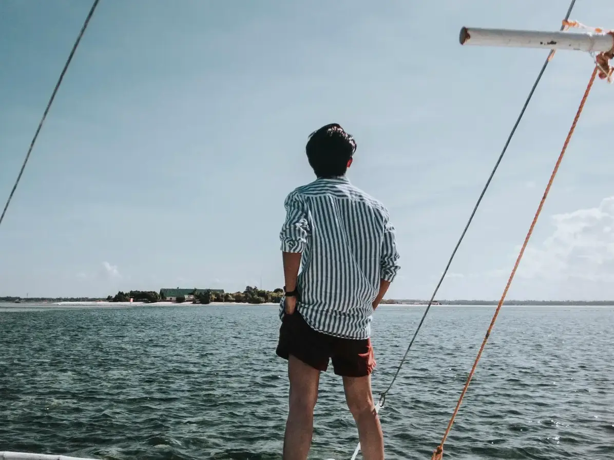 Ein Mann blickt über Bord auf eine kleine vorgelagerte Insel | Quelle: Pexels