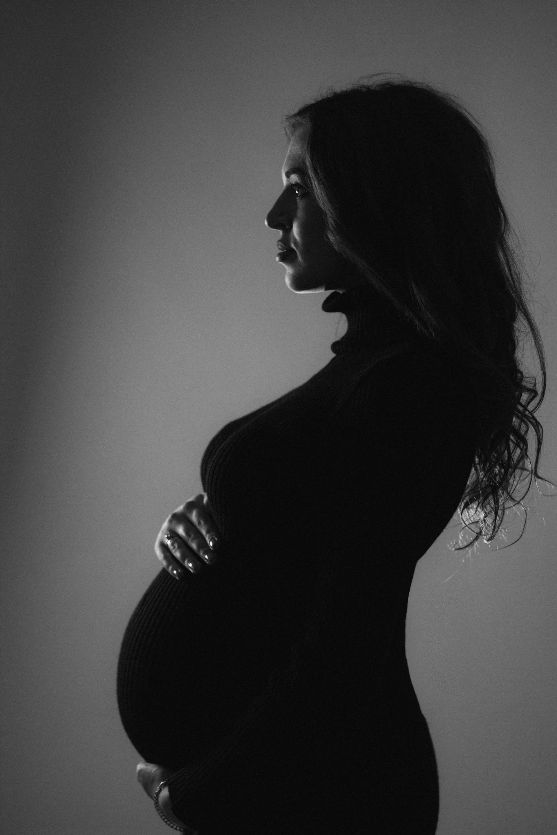 Ein schwarz-weißes Seitenprofilbild einer schwangeren Frau, die ihren Babybauch hält | Quelle: Pexels