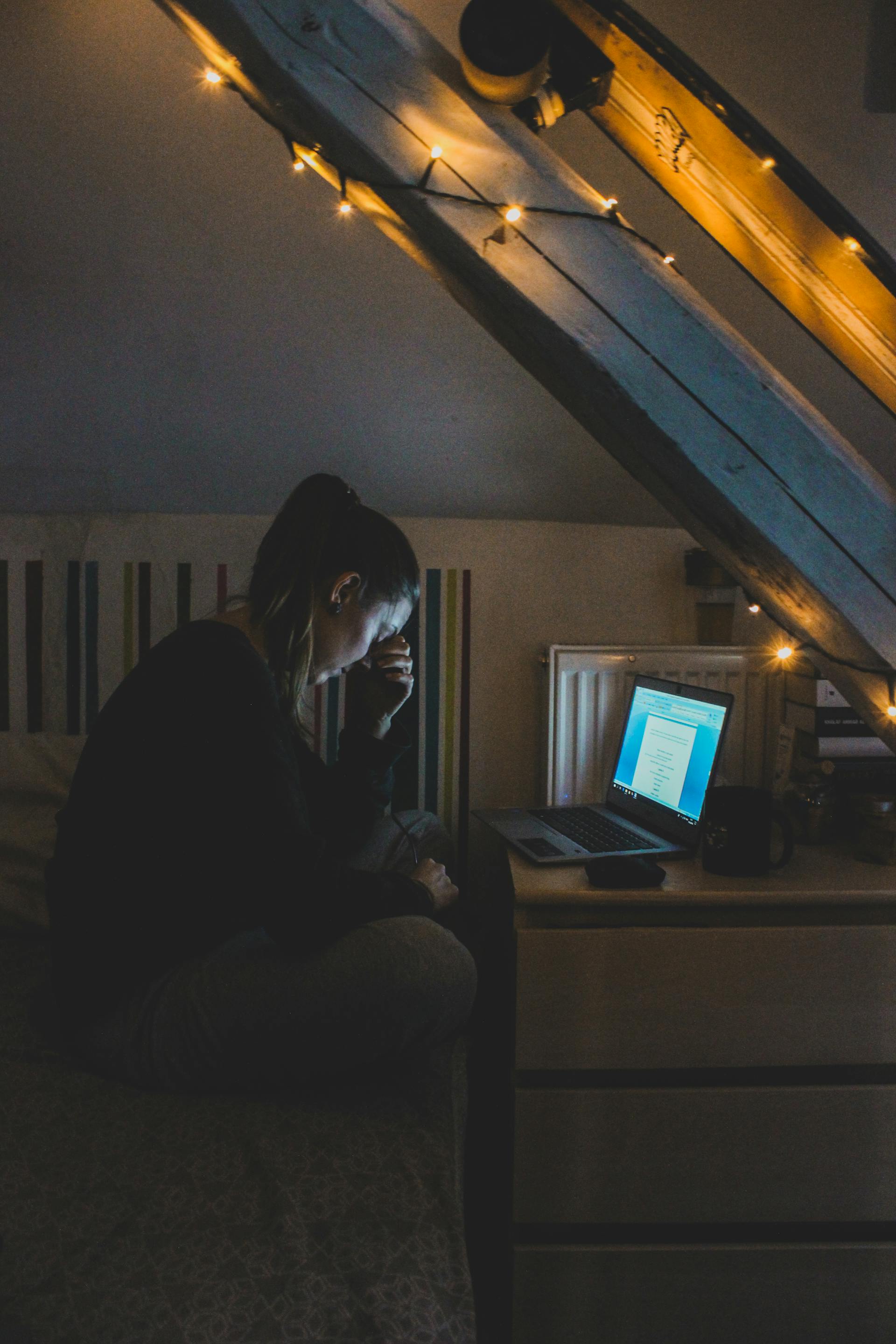 Ein mit etwas Abstand aufgenommenes Foto einer Frau, die verzweifelt aussieht, während sie nachts ihren Laptop benutzt | Quelle: Pexels