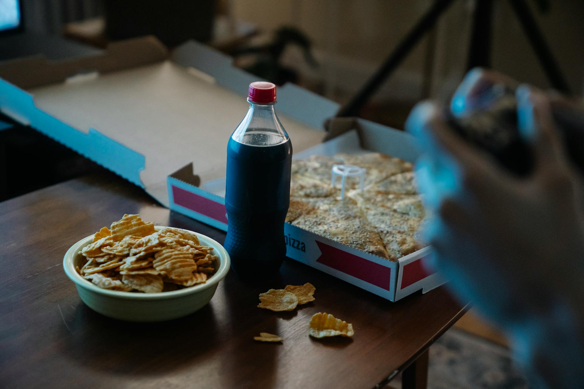 Eine Person, die Pizza, Cola und Kartoffelchips genießt | Quelle: Pexels